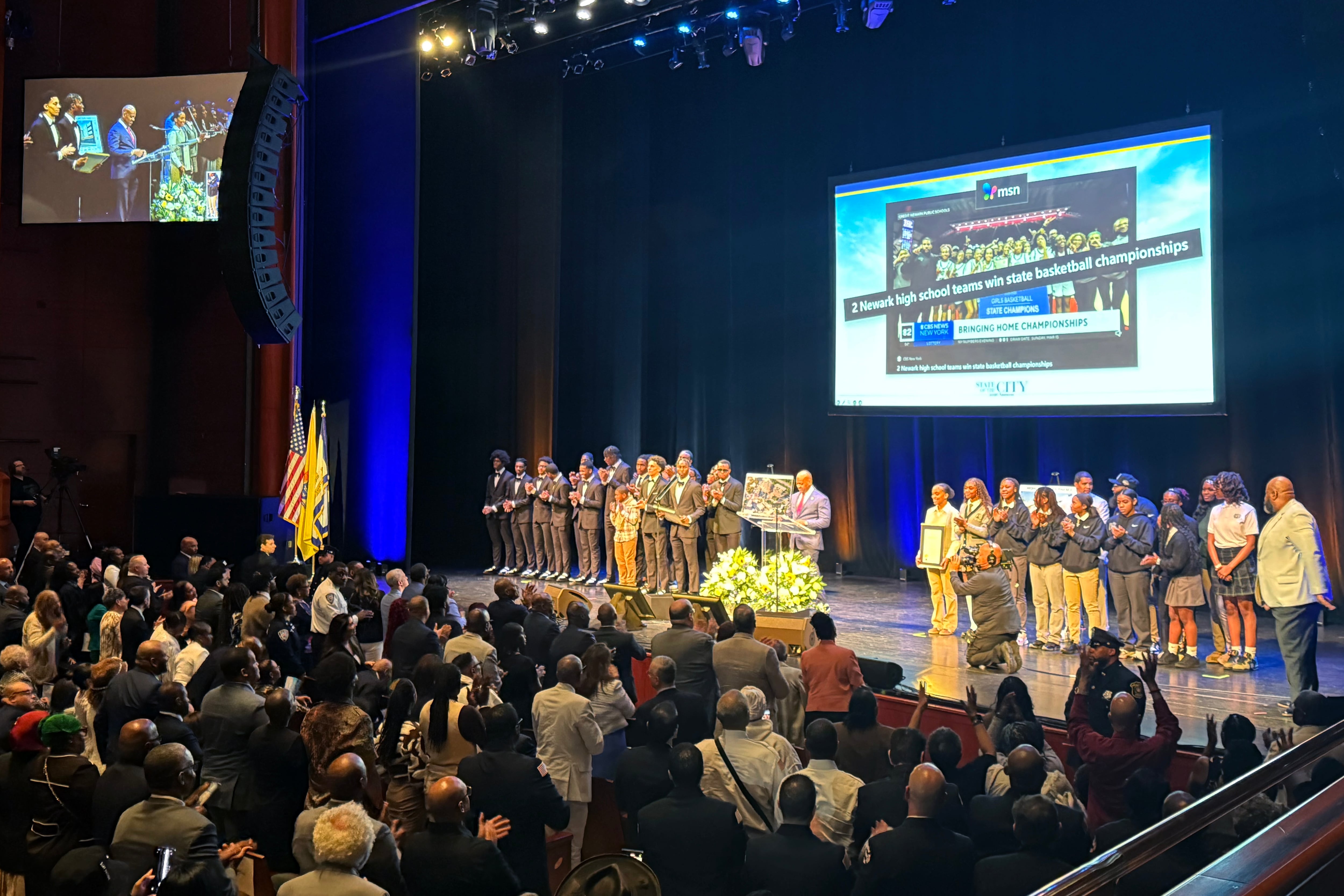 A photograph of a group of high school athletes and the Newark mayor on stage.