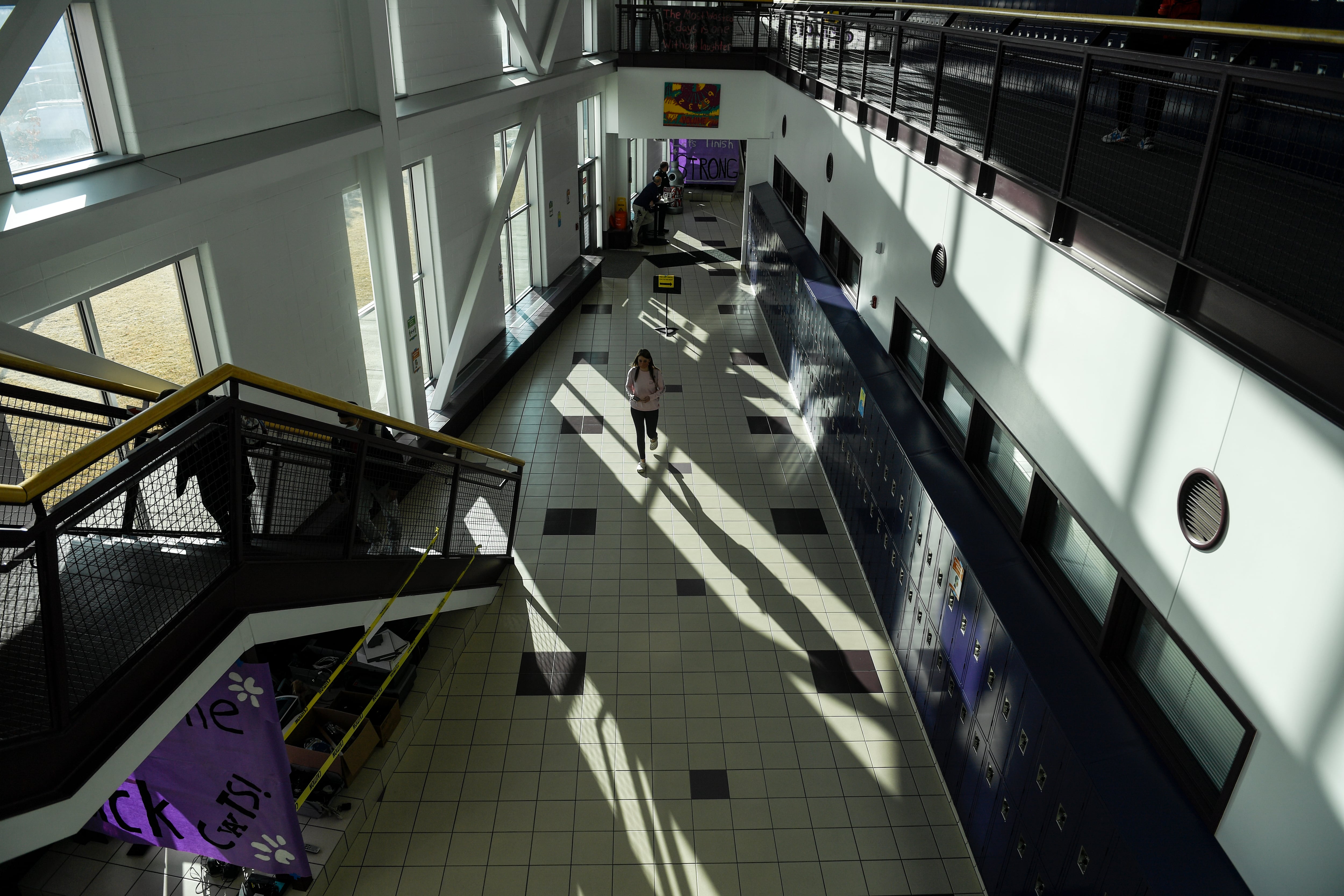 Seen from above, a masked student walks in a wide school corridor.