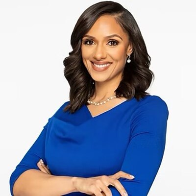 A photograph of a Black woman with short dark hair and smiling while wearing a blue dress against a white background.