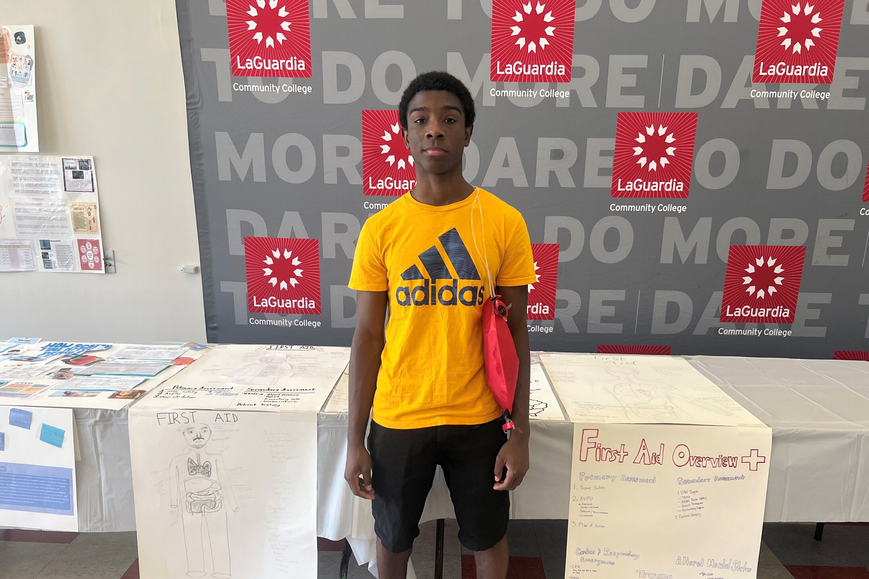 A rising senior teen poses for a portrait in front of a folding table and a large grey sign with red square logos.