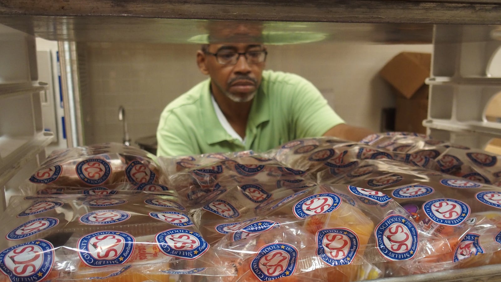 Kevin Patterson, a cafeteria supervisor at Kirby High School, prepares meals for lunch during a summer session.