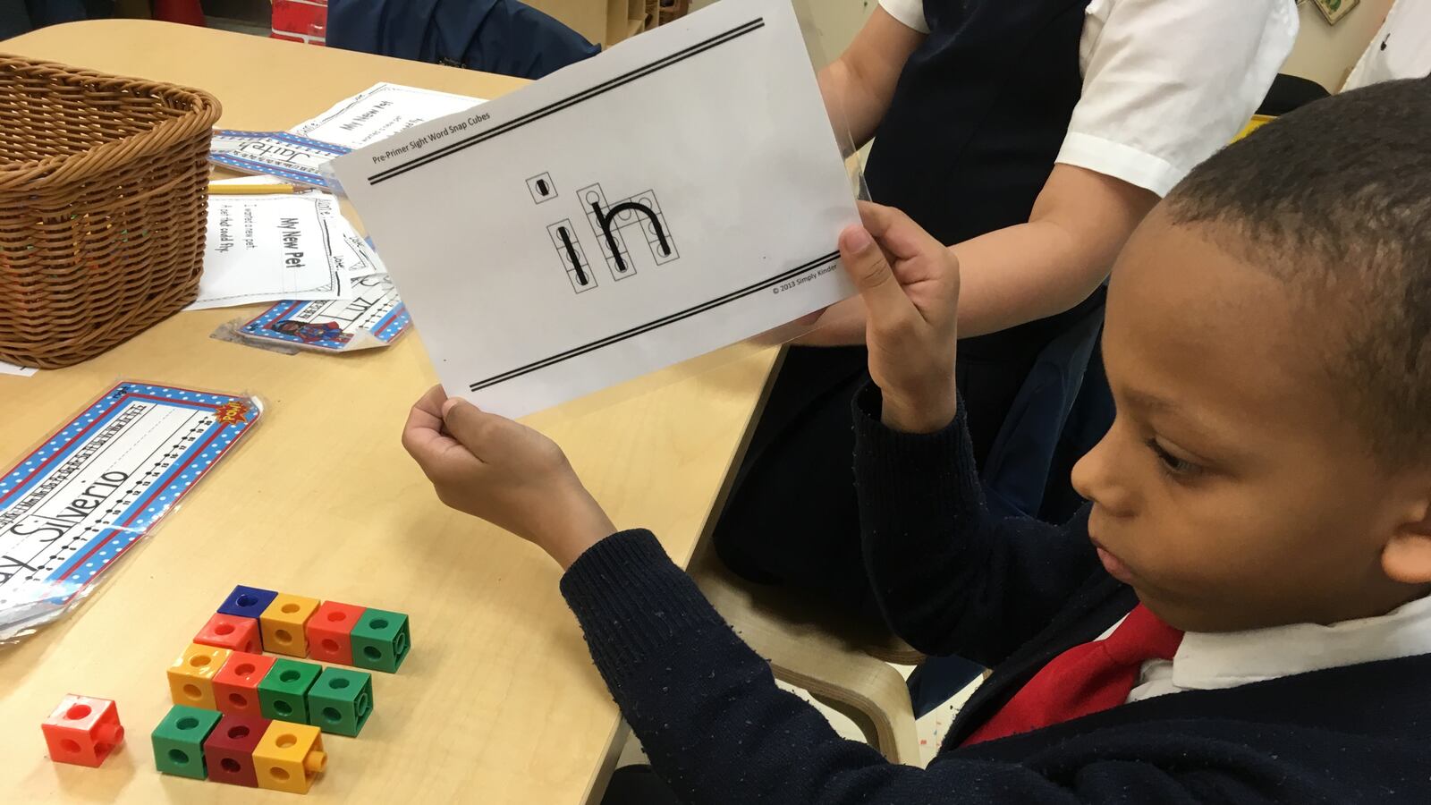 A kindergartener re-creates a flashcard word using Unifix cubes — a hands-on way to reinforce reading skills.