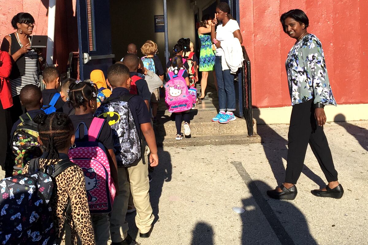 A line of students wearing backpacks walks into an elementary school.