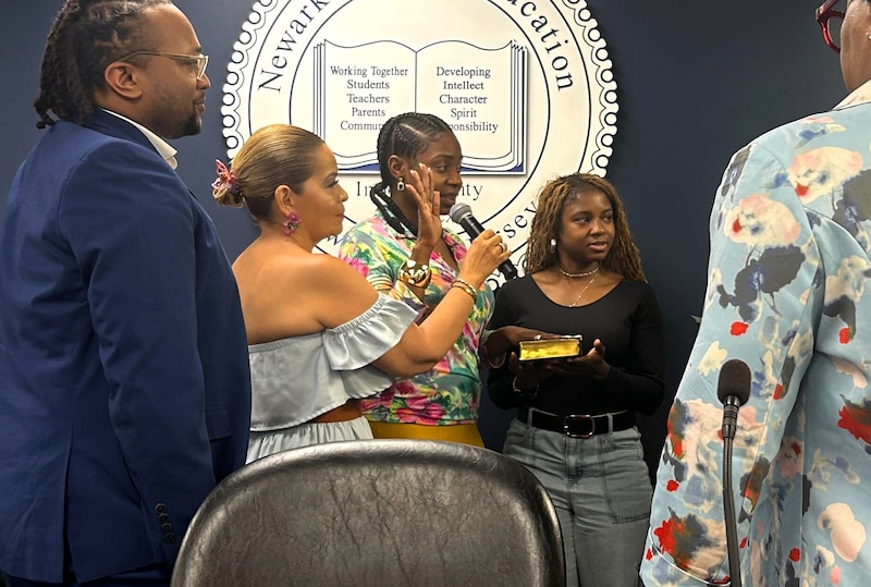 A woman in a brightly colored blouse holds her hand up and is surrounded by others.