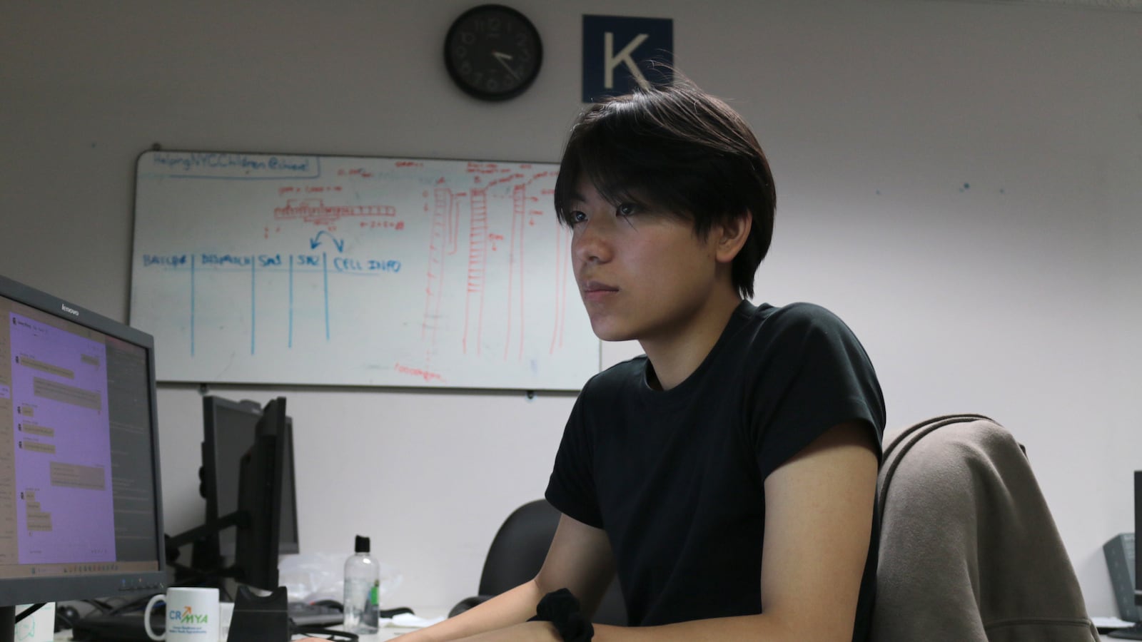 A student in a black shirt sits at a computer in a classroom.
