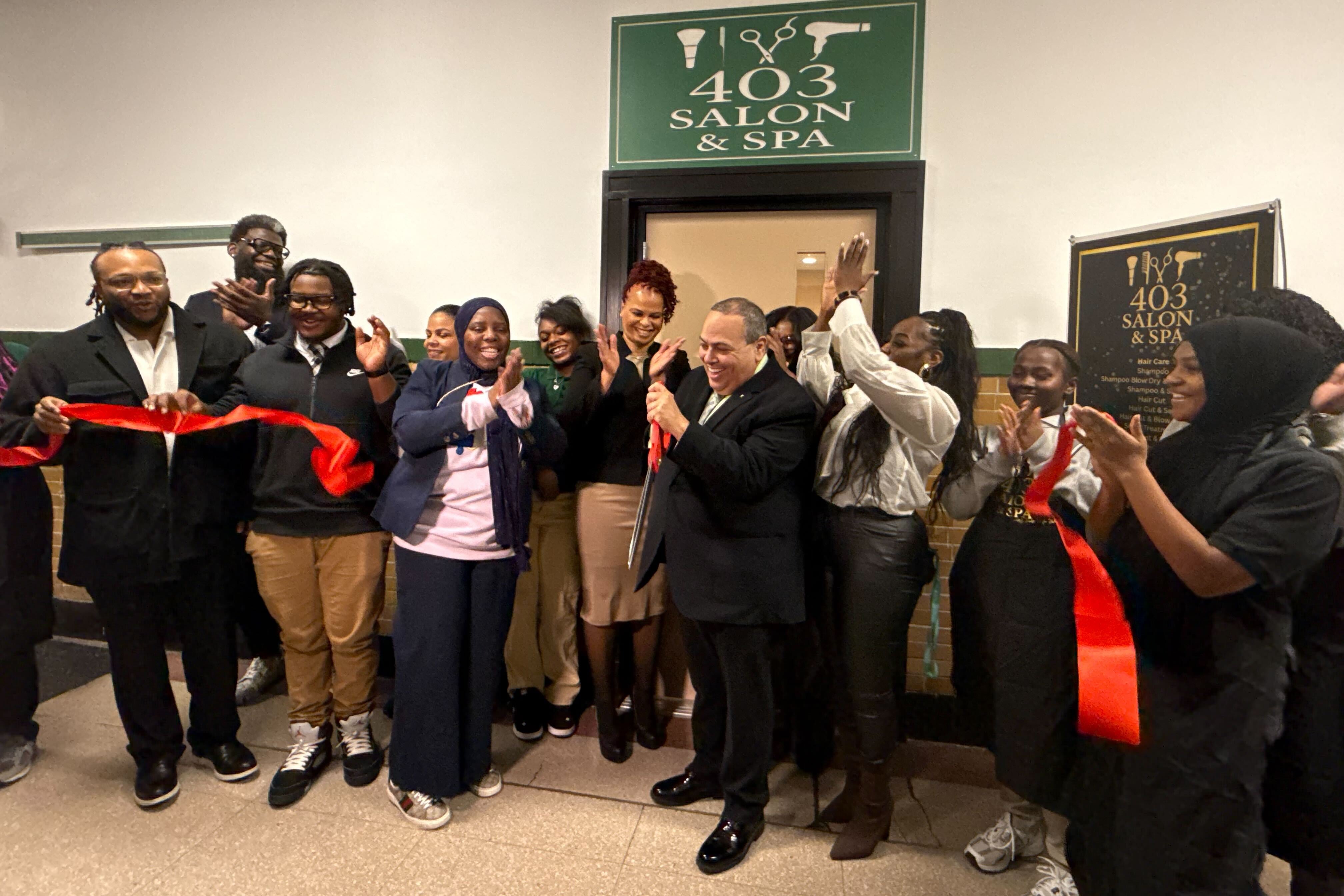A group of people cheer and raise their hands outside a salon and spa after cutting a red ribbon.