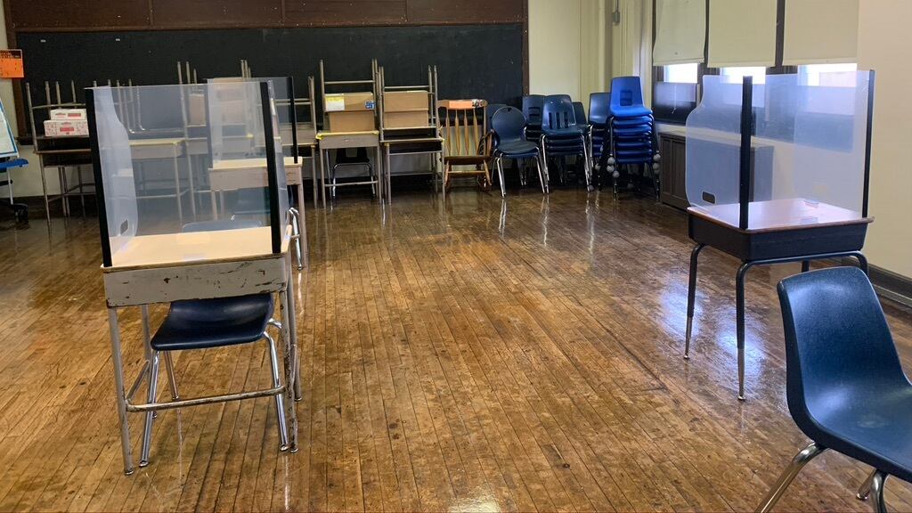 Classroom of desks spaced 6 feet apart with shields on top of the desks.