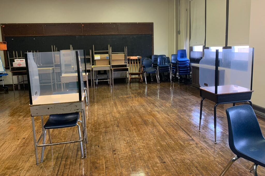 Classroom of desks spaced 6 feet apart with shields on top of the desks.