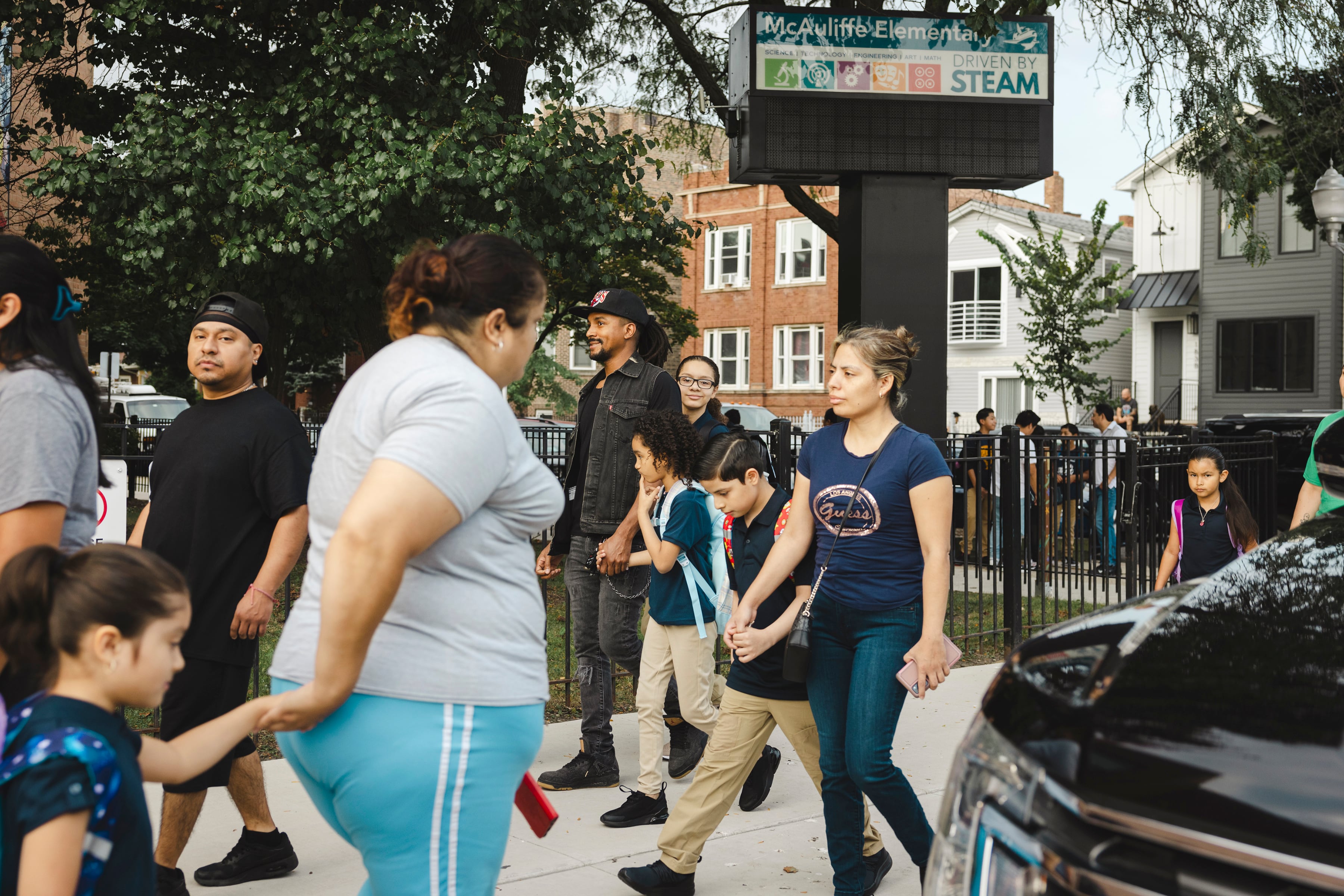 Adults and young students walk to and from the entrance of a school building.