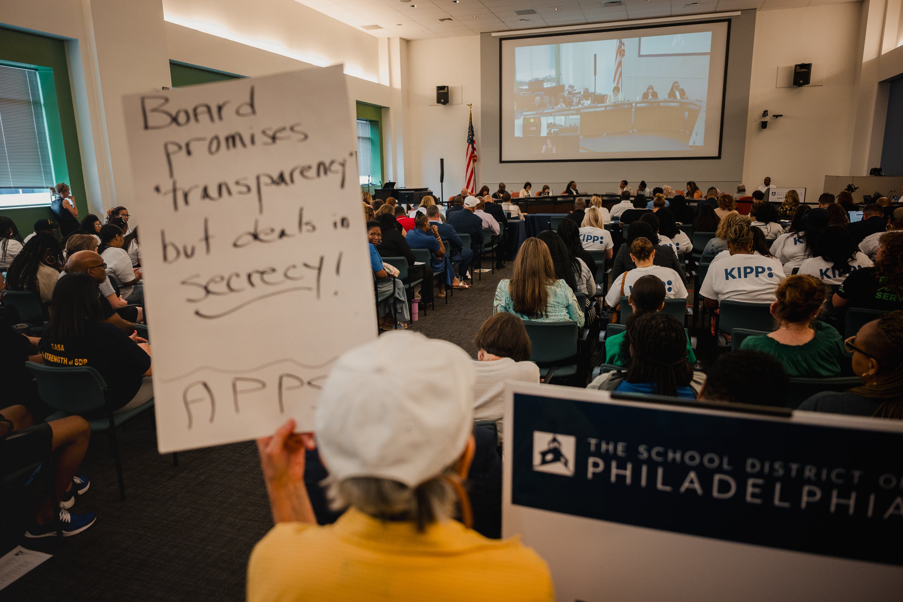 A woman in yellow holds a sign in a crowded meeting.