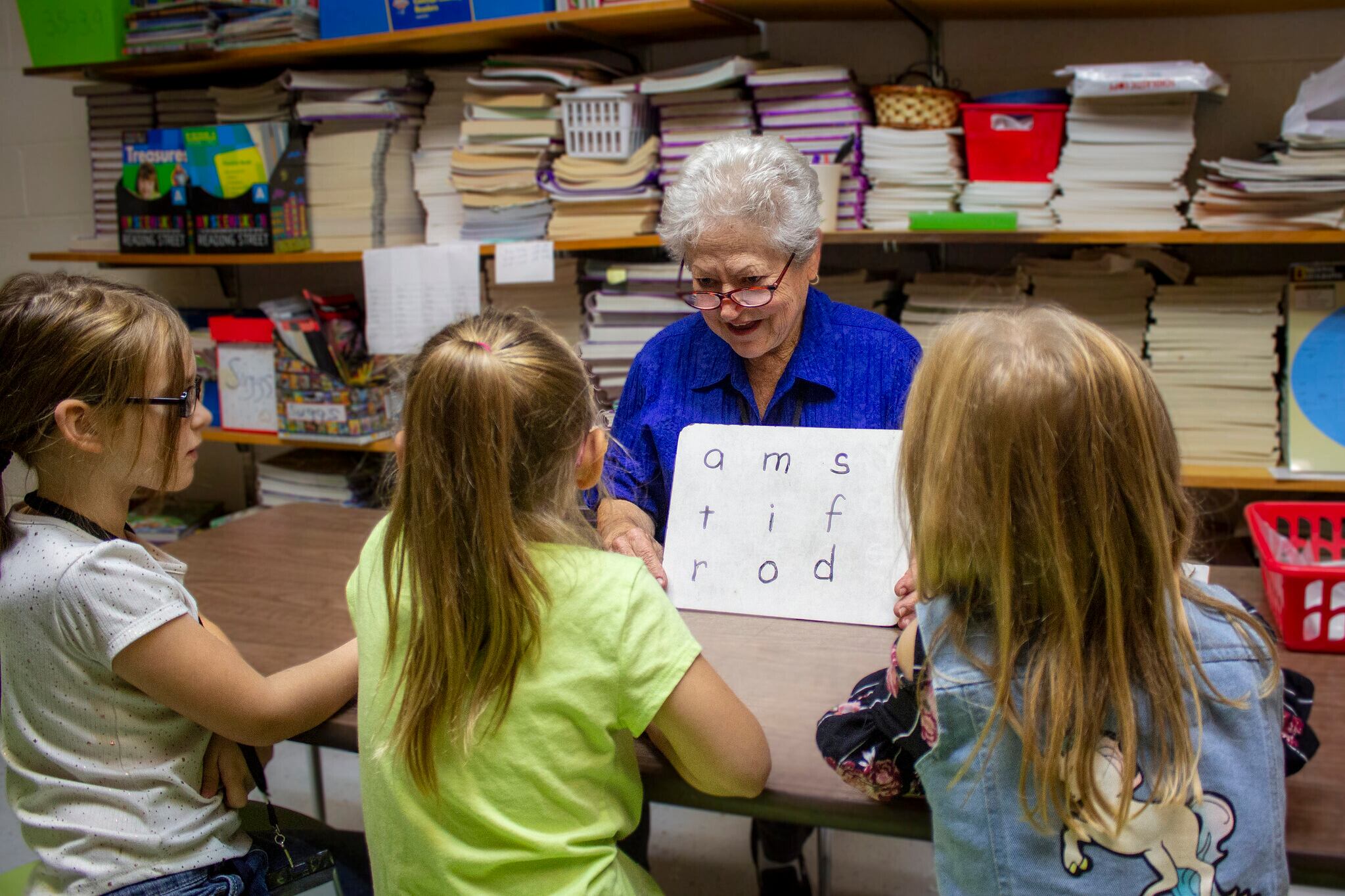 a woman in a blue top and glasses works with three young female students.