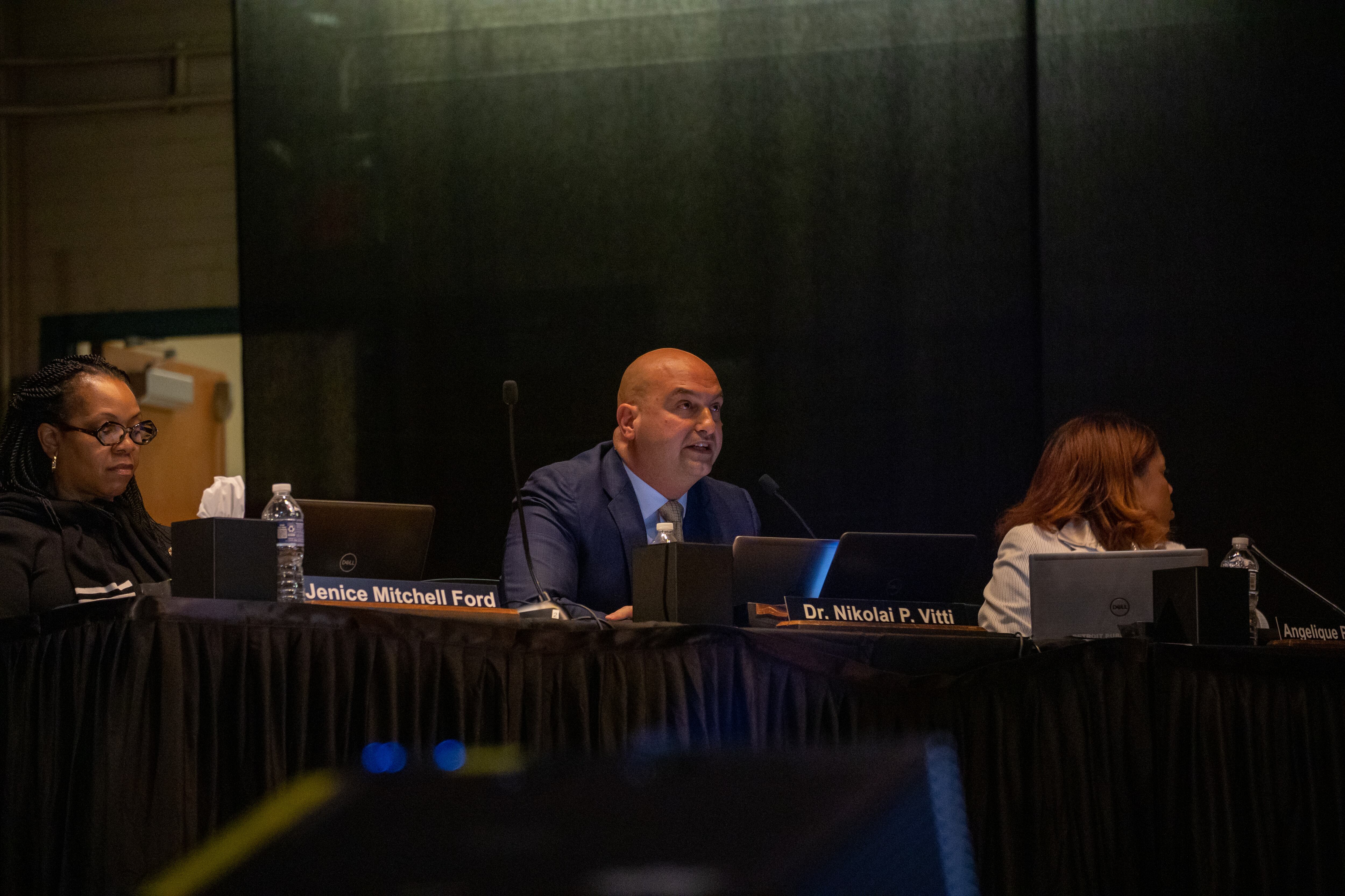A person in a suit speaks on a school auditorium