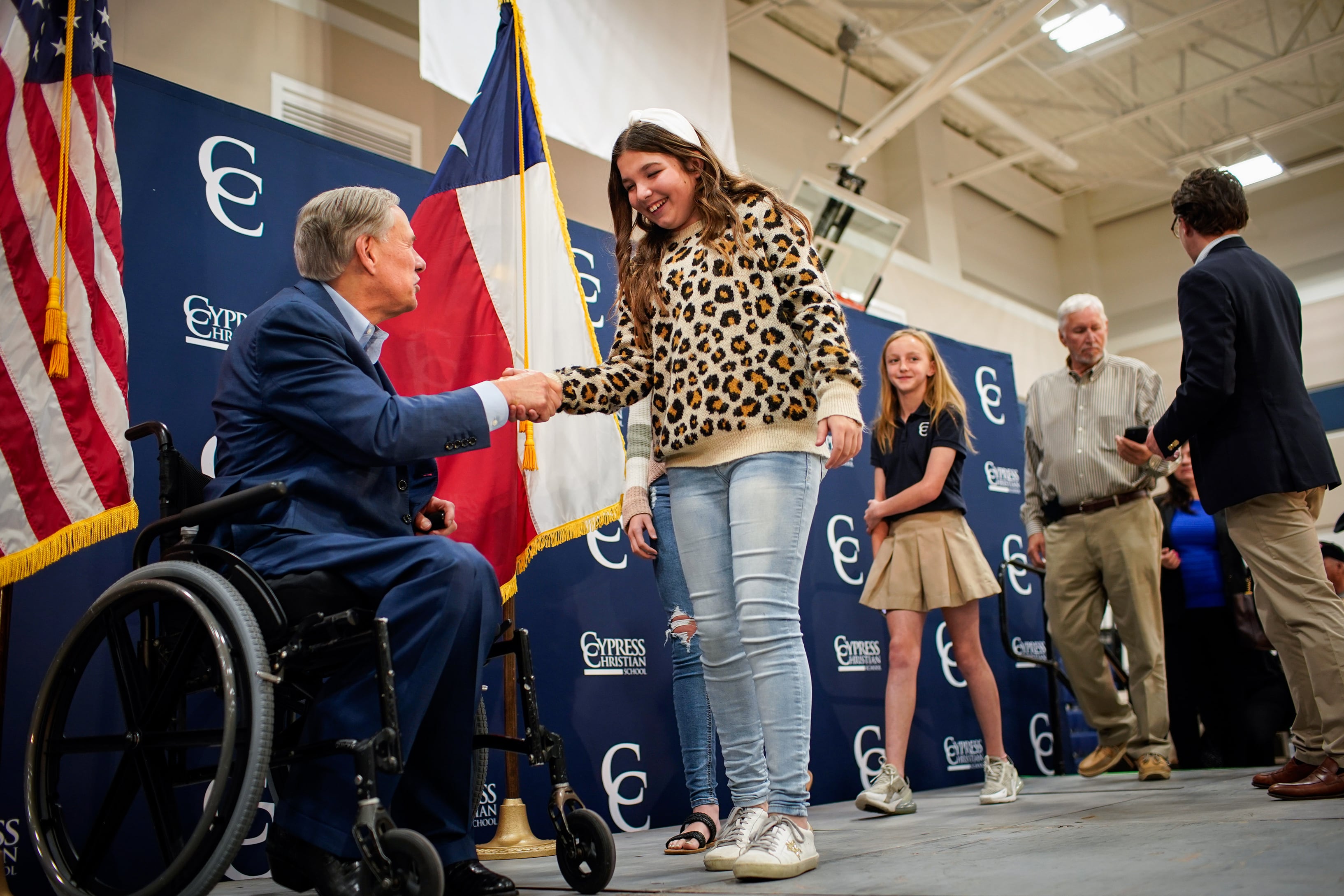 A man in a suit and sitting in a wheelchair shakes a hand with a student.