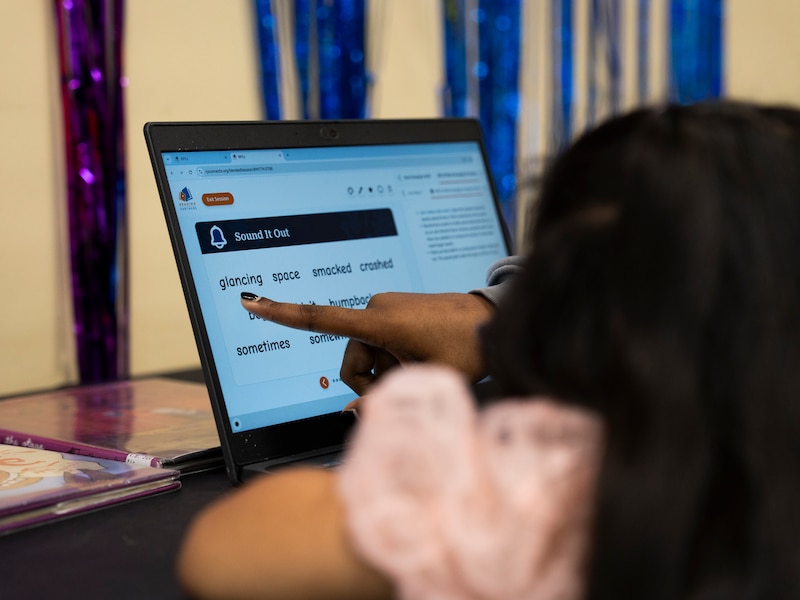 A finger is pointing at the laptop's screen.
