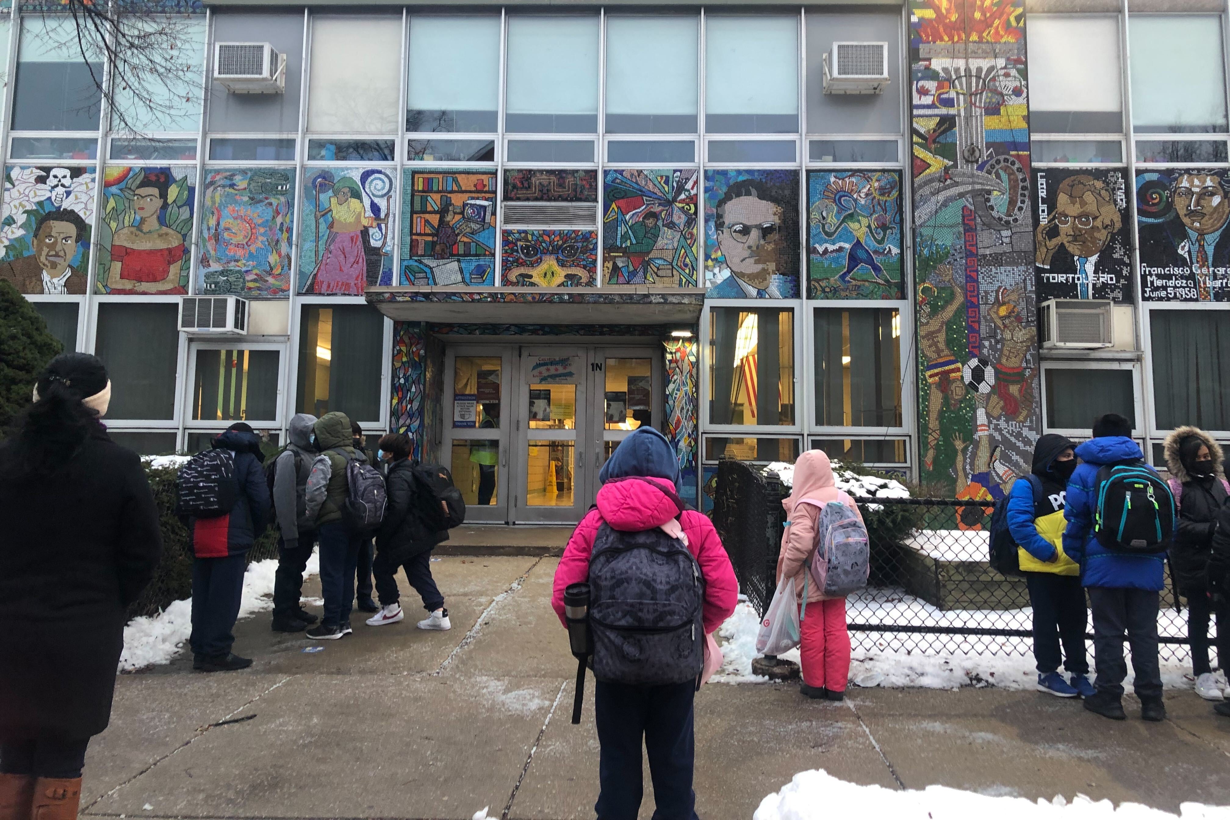 Students, wearing masks and carrying backpacks and accompanied by parents, line up along outside Cooper Elementary in Pilsen.