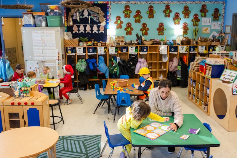 A group of students and teachers sit at tables in a classroom.
