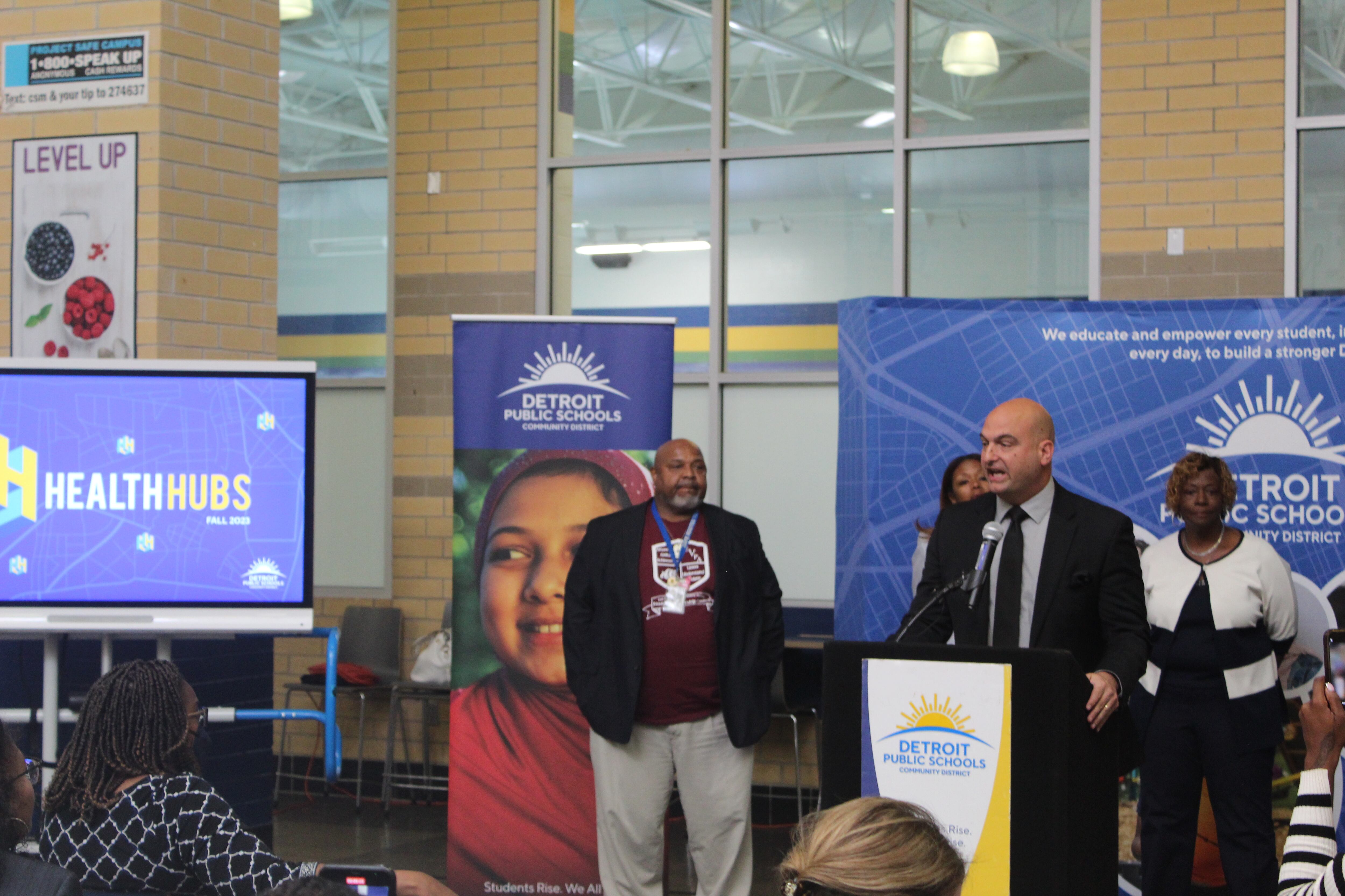 A person speaks at a podium while three people stand behind him.