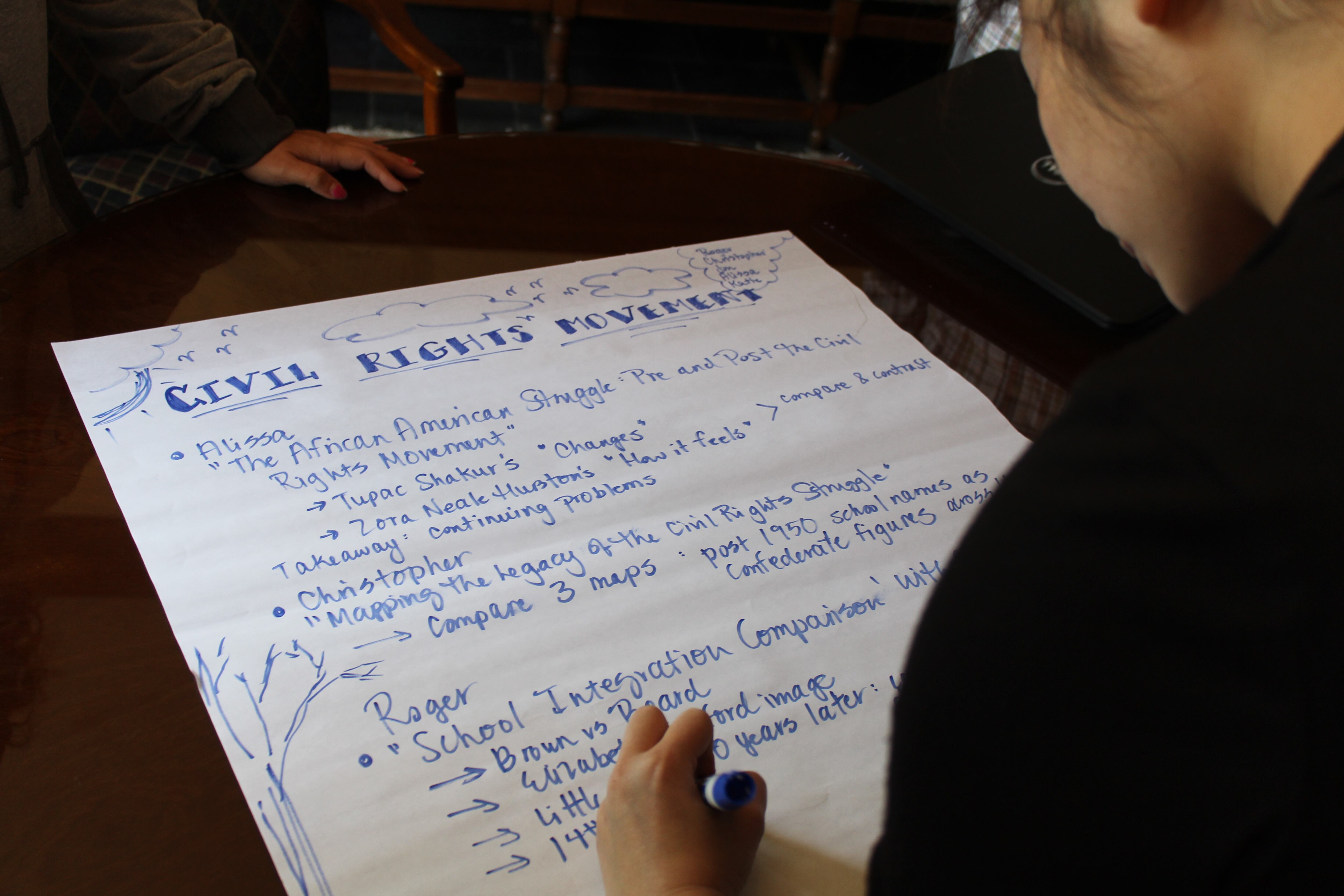 A high school history teacher writes down lesson plans that her team will present to the group.