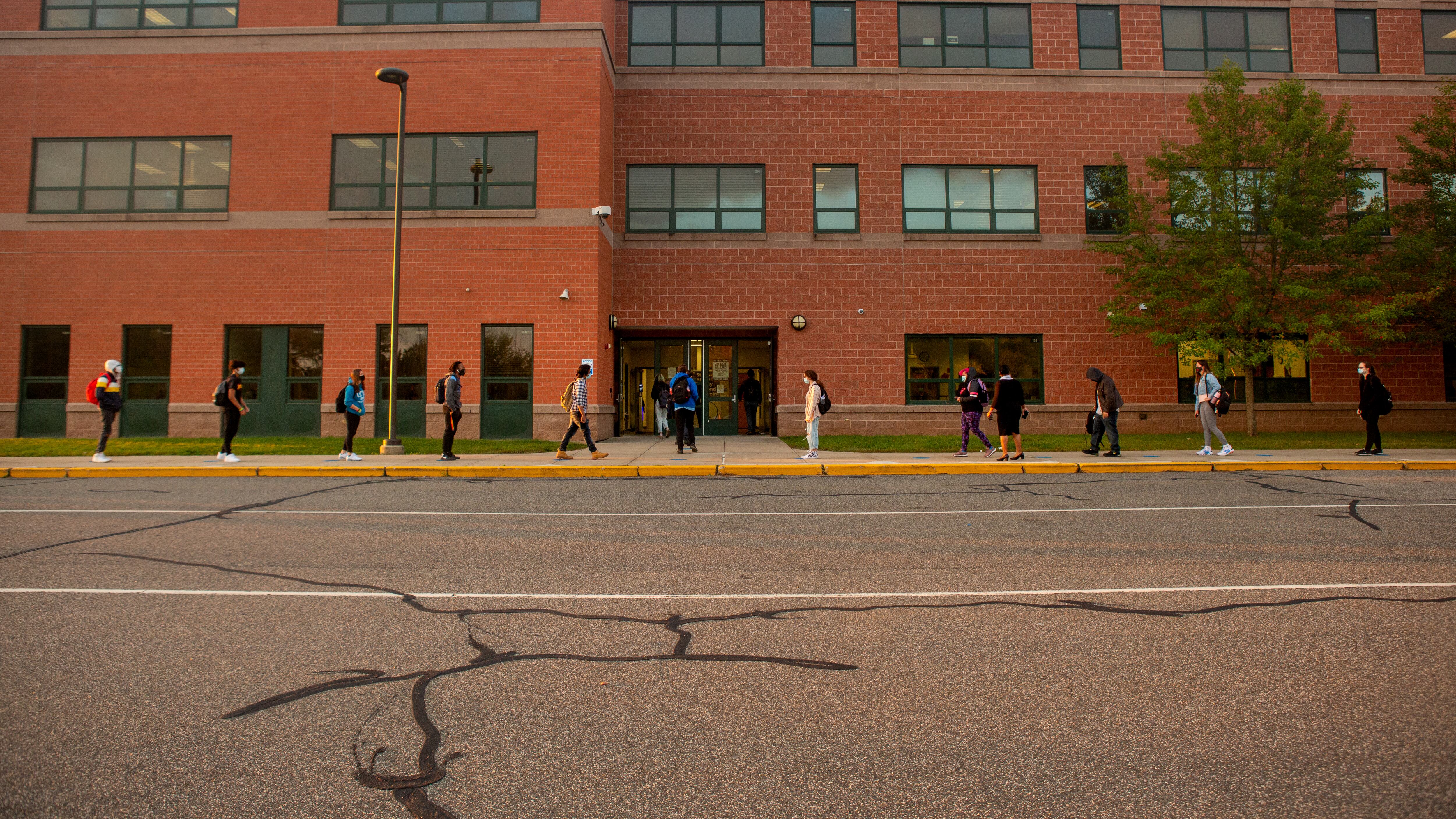 Students line up on socially distanced dots painted on the sidewalk to wait their turn to be scanned by a temperature screener before classes.