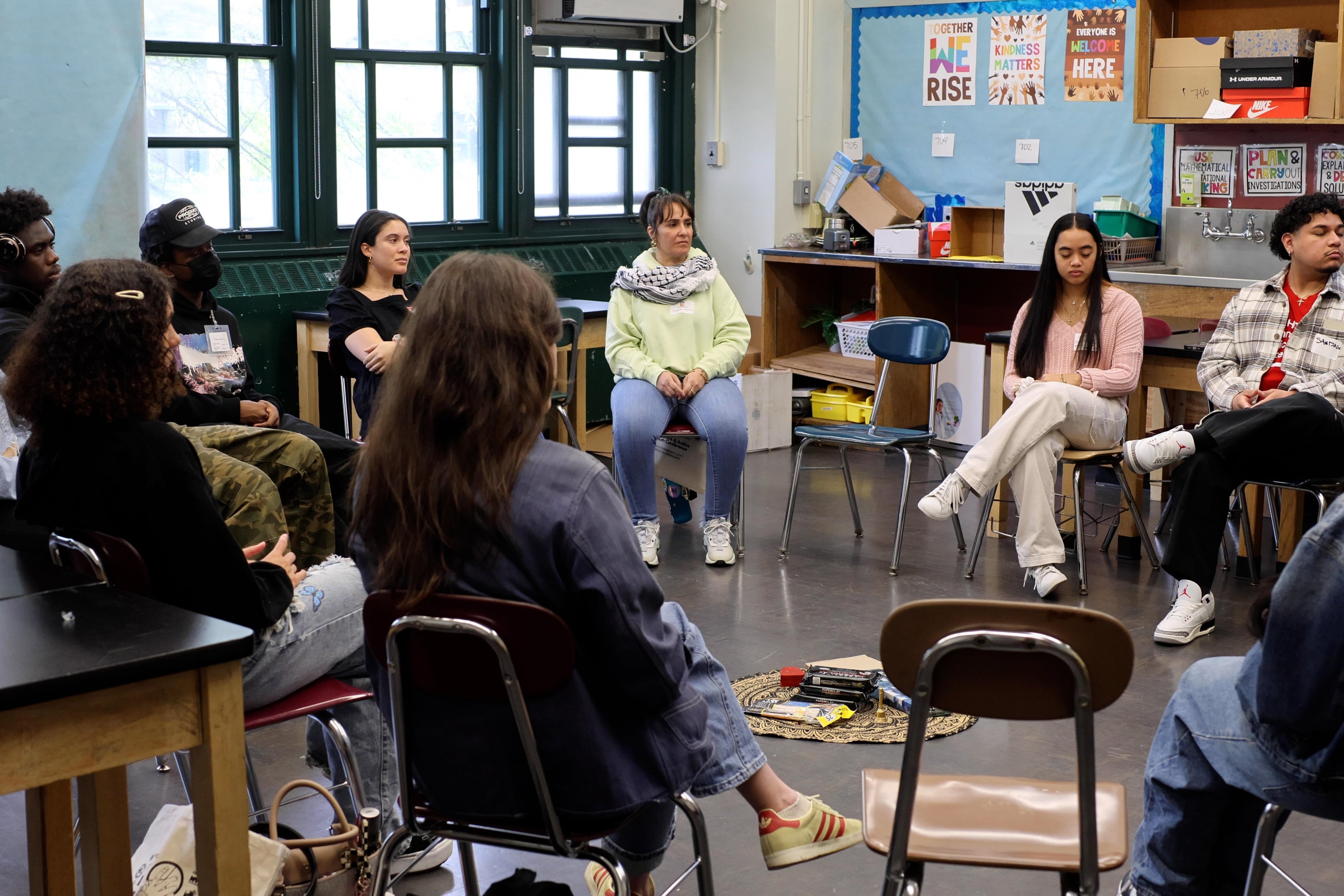 A group of high school students sit in a circle in a classroom.