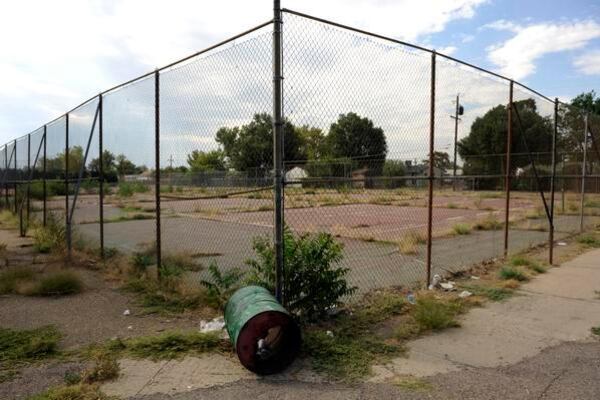 The corner of a chain link fence enclosing pavement and weeds at the former Adams City High School in Adams County, Colo.