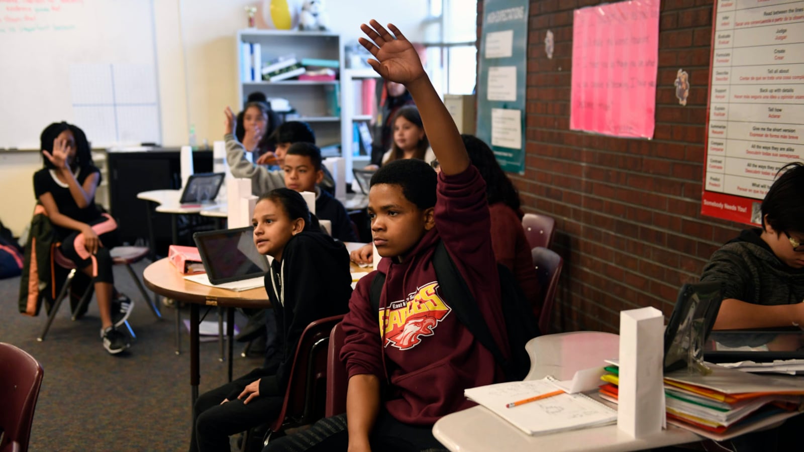Russell Patton, hand raised high, waits to be called on during Ines Barcenas’ sixth grade math class in March 2018 at East Middle School in Aurora.