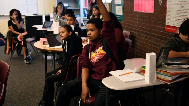 Russell Patton, hand raised high, waits to be called on during Ines Barcenas’ sixth grade math class in March 2018 at East Middle School in Aurora.