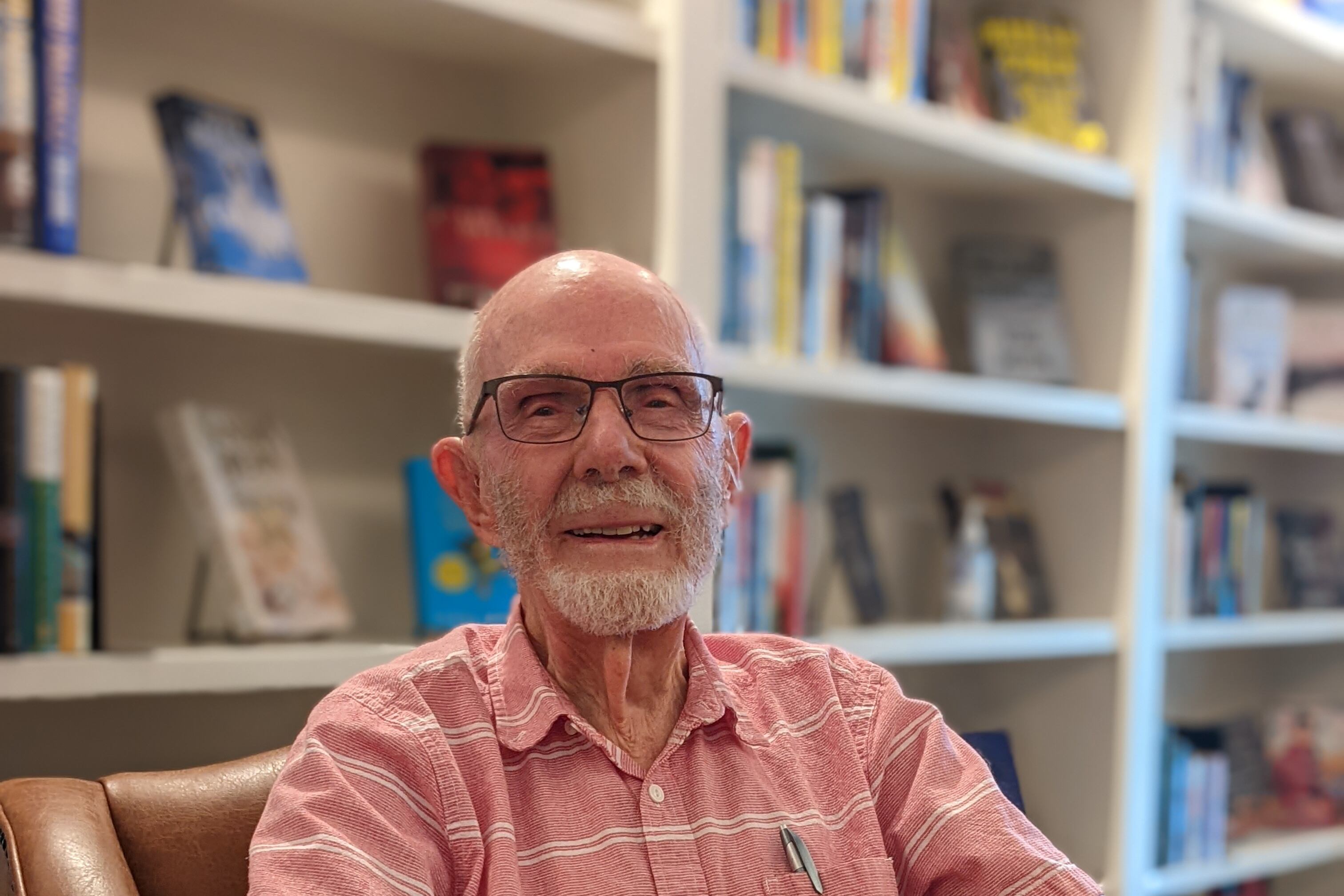 David Delaplane, dressed in a pink button up with stripes, poses for a picture with books in the background.