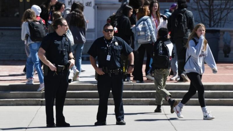 Two police officers stand outside Denver’s East High School as students walk in the background.