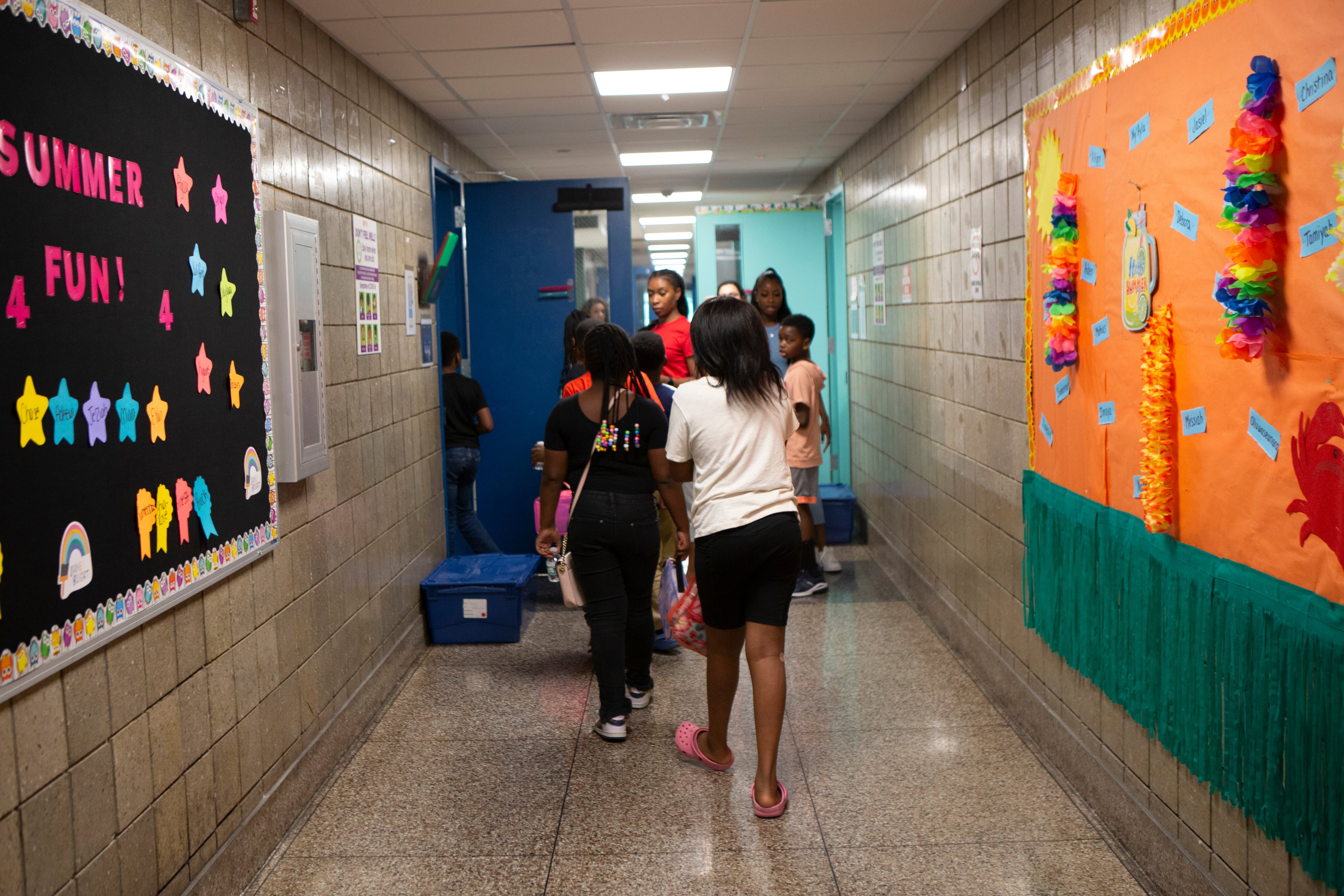 A group of students and faculty walk down a hallway with posters and decorations on the walls.