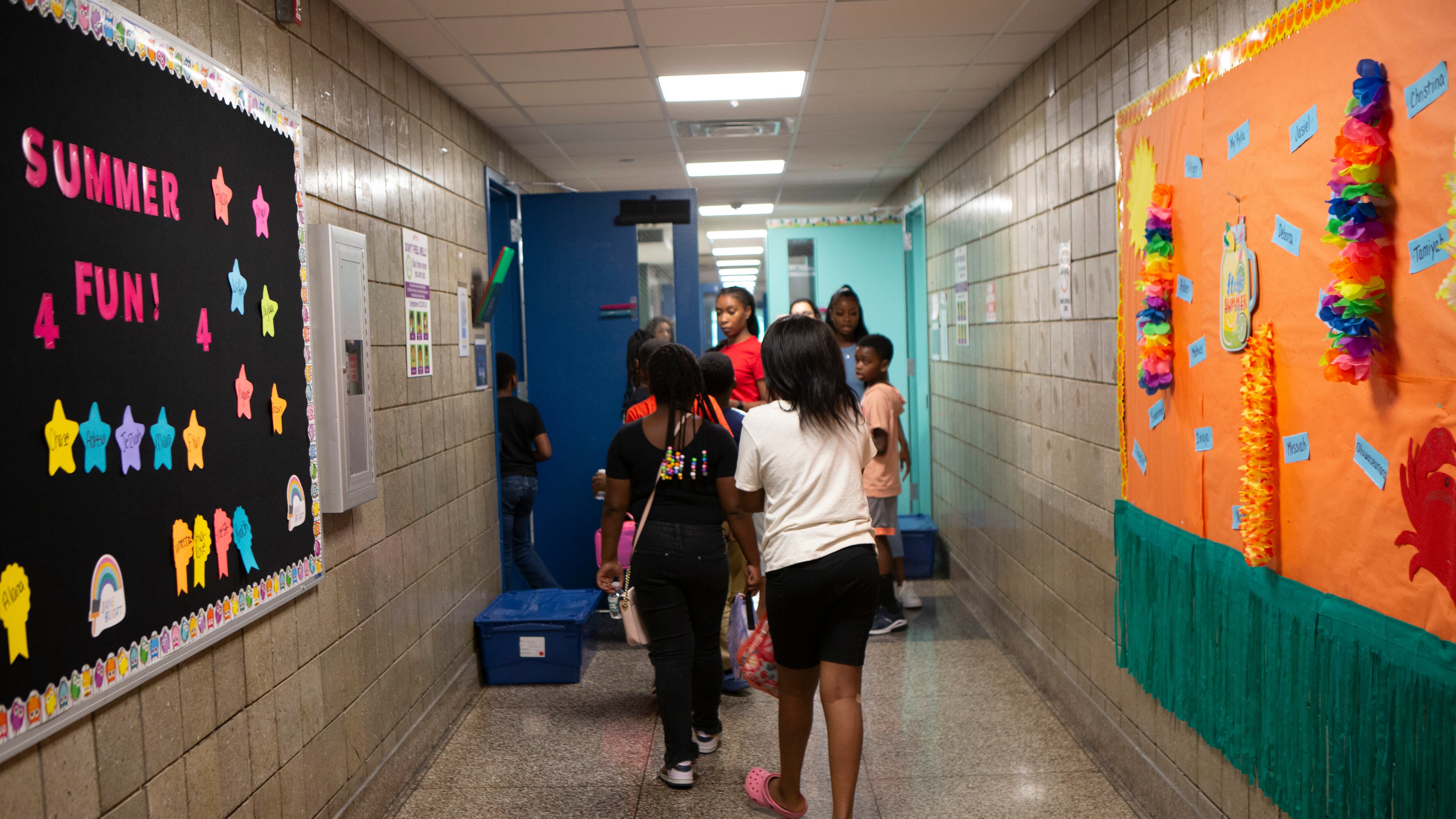 A group of  students and faculty walk down a hallway with posters and decorations on the walls.