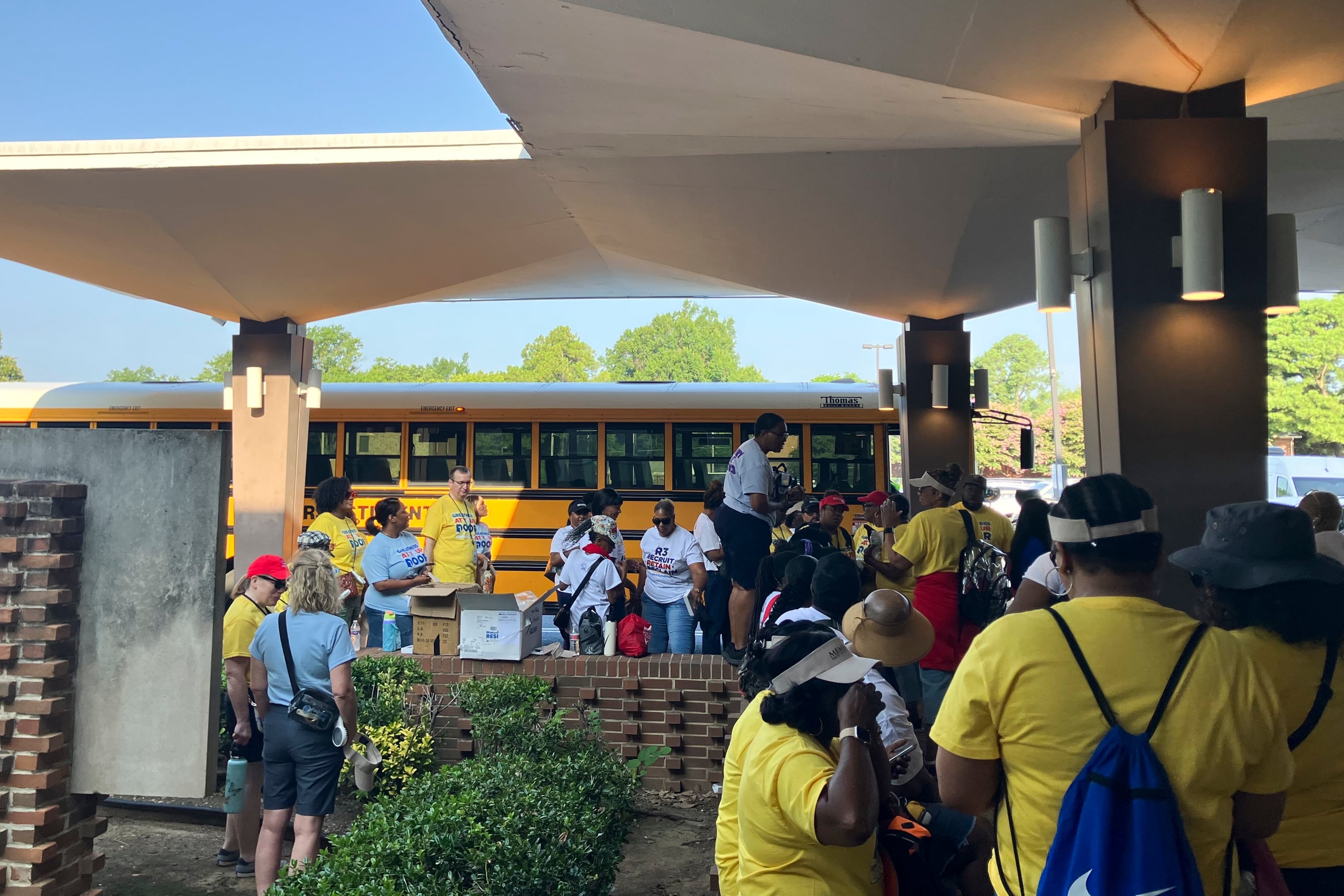A group of people wearing white and yellow shirts standing next to a yellow school bus.