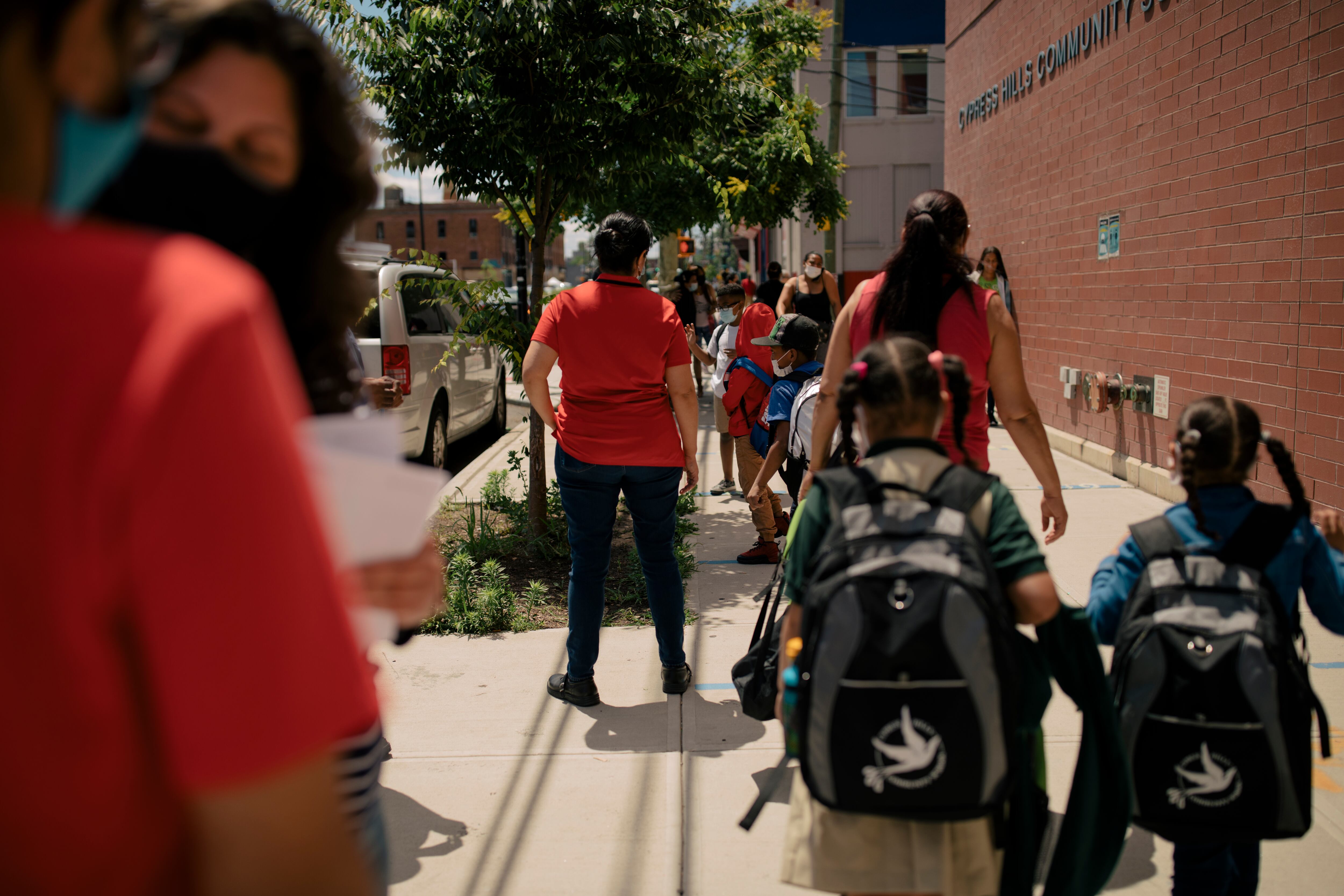 Two students wearing backpacks line up outside a brick school building.