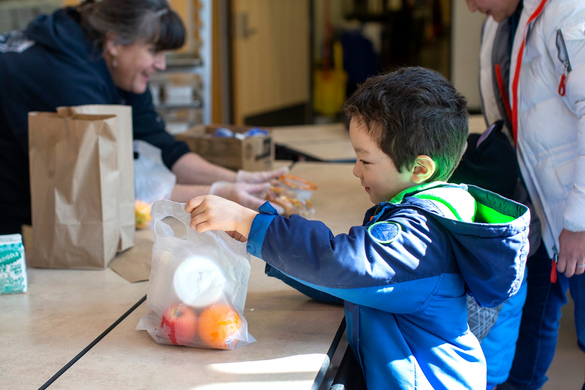 A young student smiles while grabbing a plastic bag full of fruit and food.