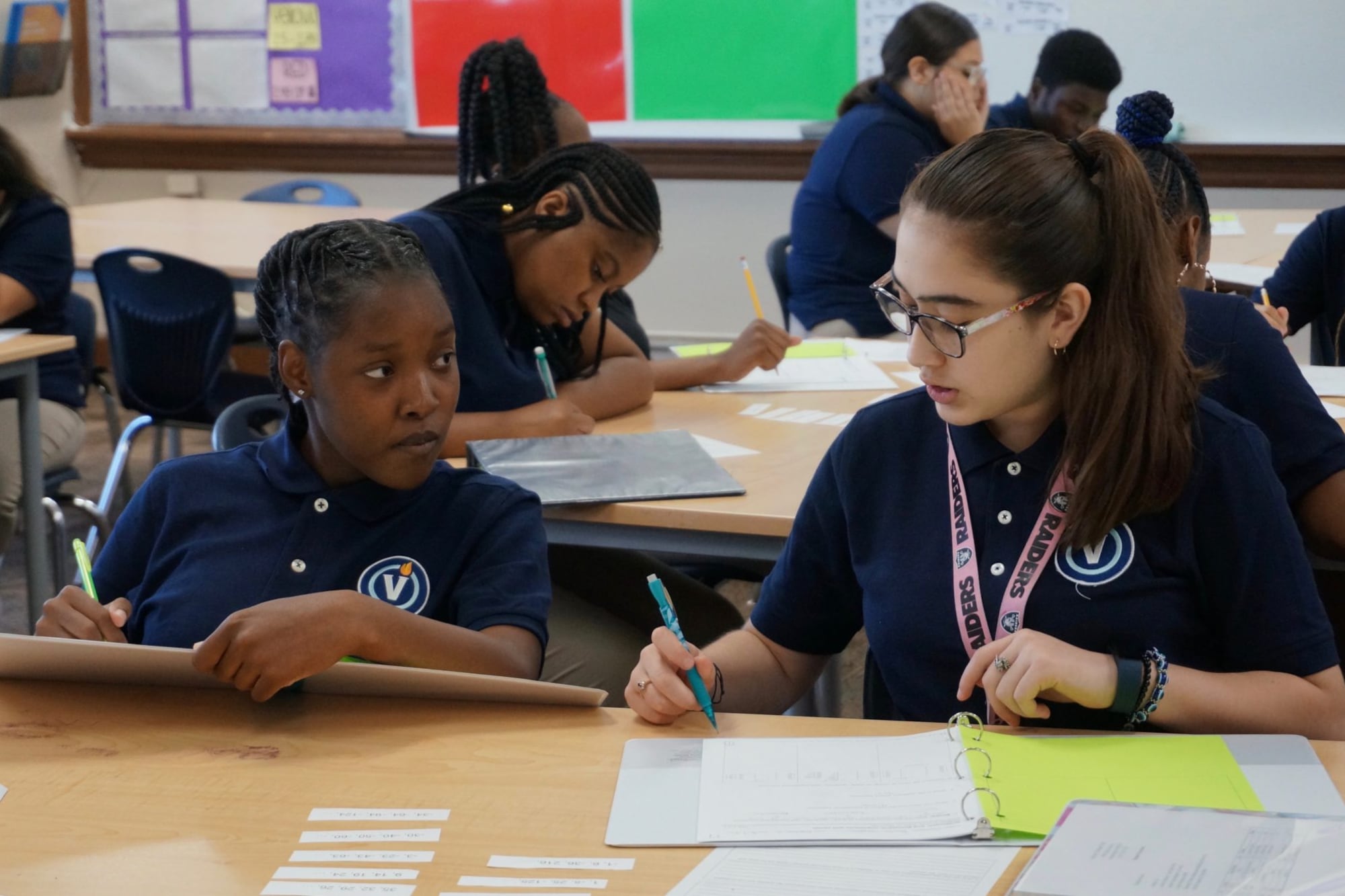Two people wearing blue shirts sit at a desk.