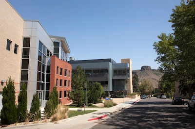 Buildings of various sizes and colors line the left of a street with the Castle Rock formation in the background with blue skies.