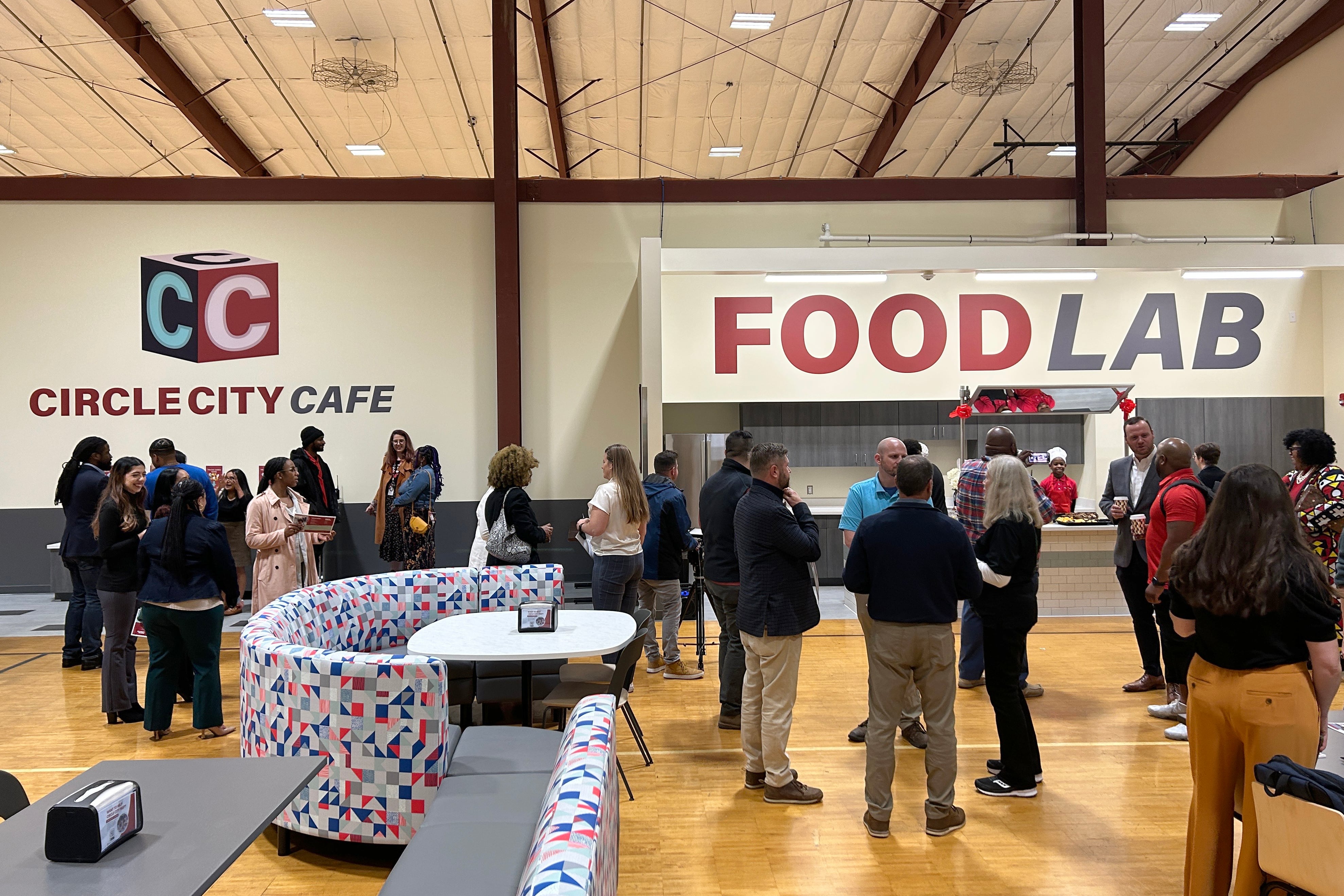 a photograph of a large school gym with adults and students spread out.