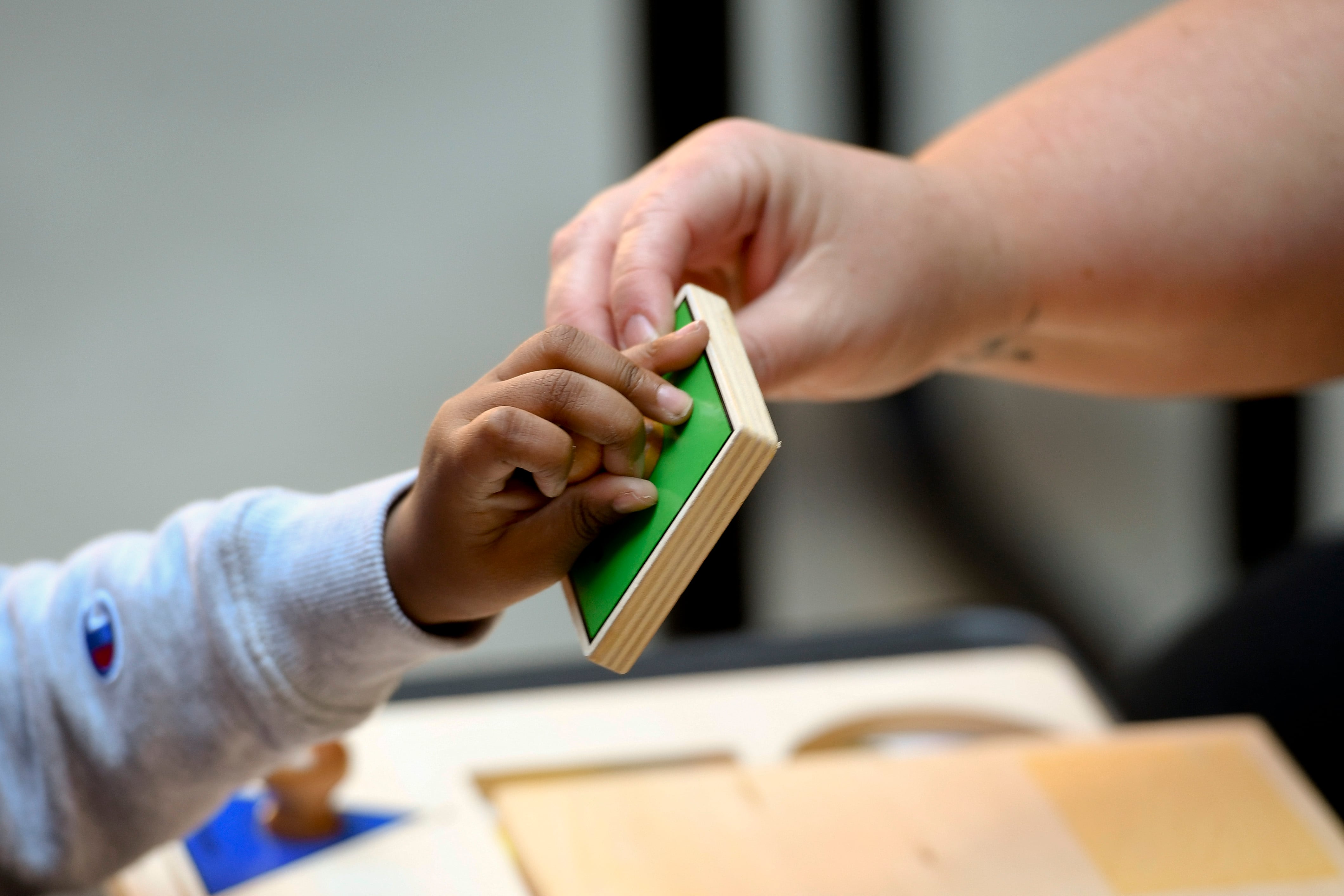 A child's hand and an adult hand hold a green block.