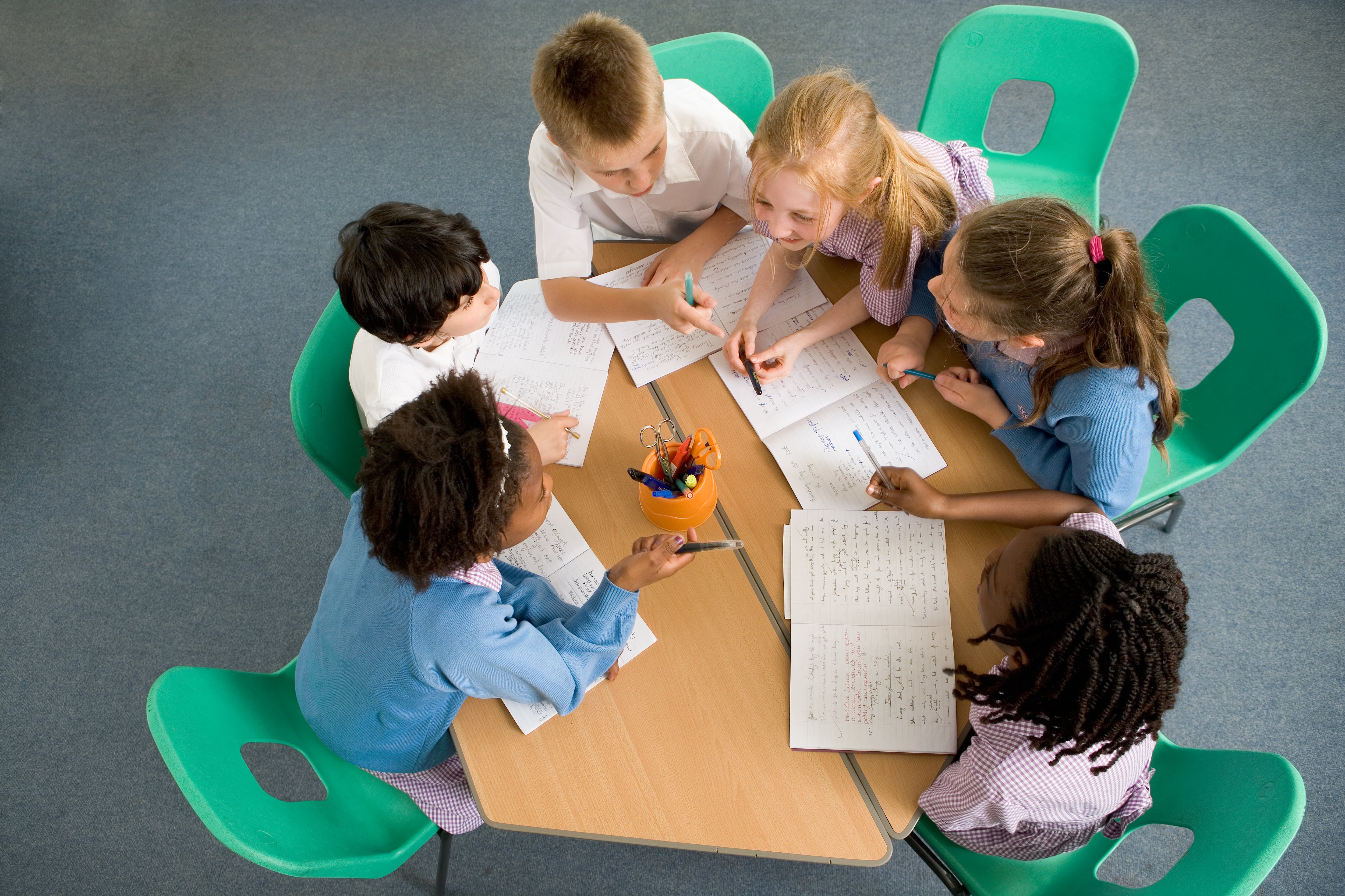 Children (7-12) sitting around table, having discussion, elevated view - stock photo