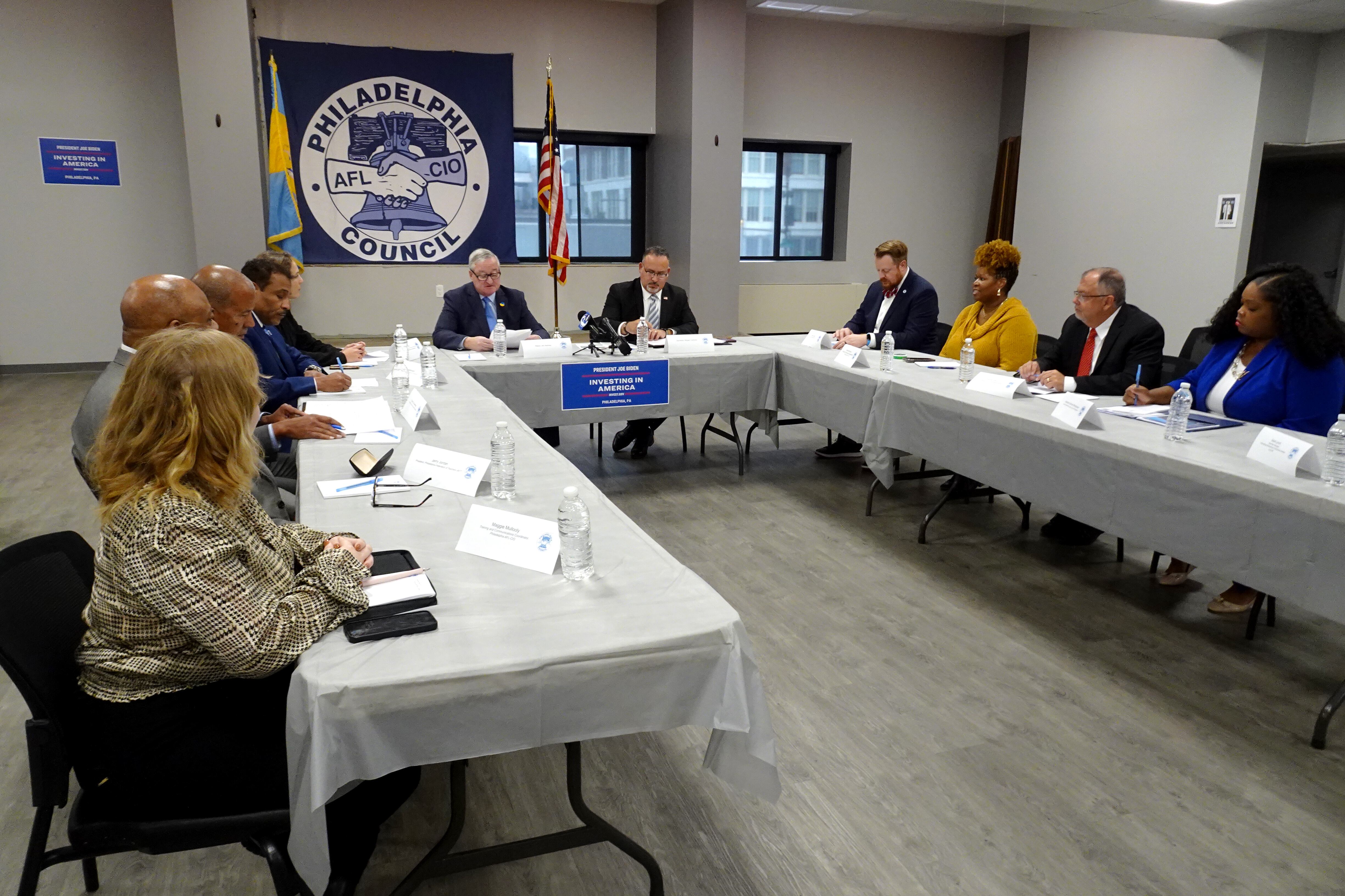 A group of people including U.S. Education Secretary Miguel Cardona sit around a series of tables in a “U” formation