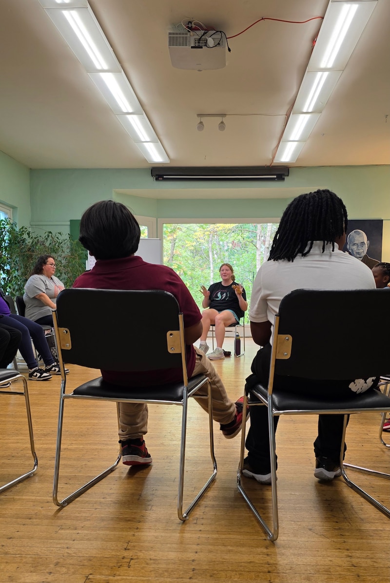 A photograph of two students sitting in chairs with an adult in the background.