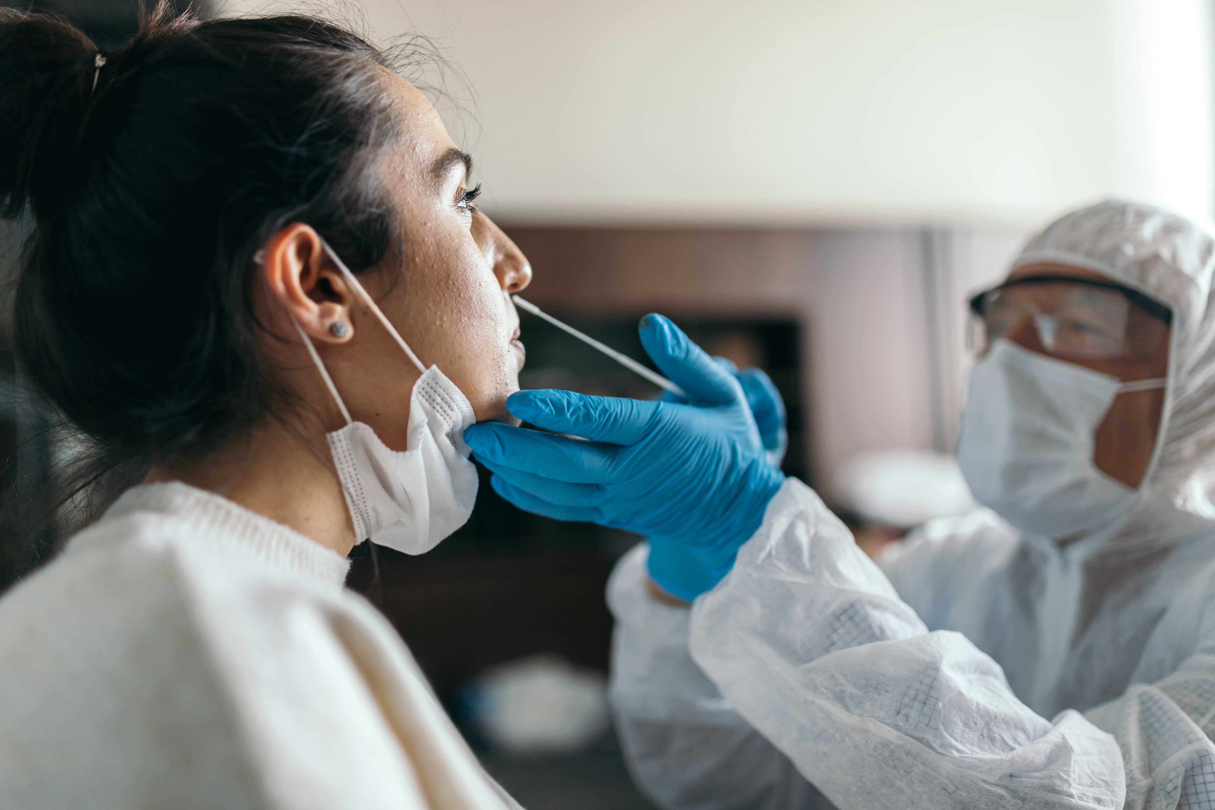 A young woman receives a nose swab from a medical professional wearing a full protective suit and mask.
