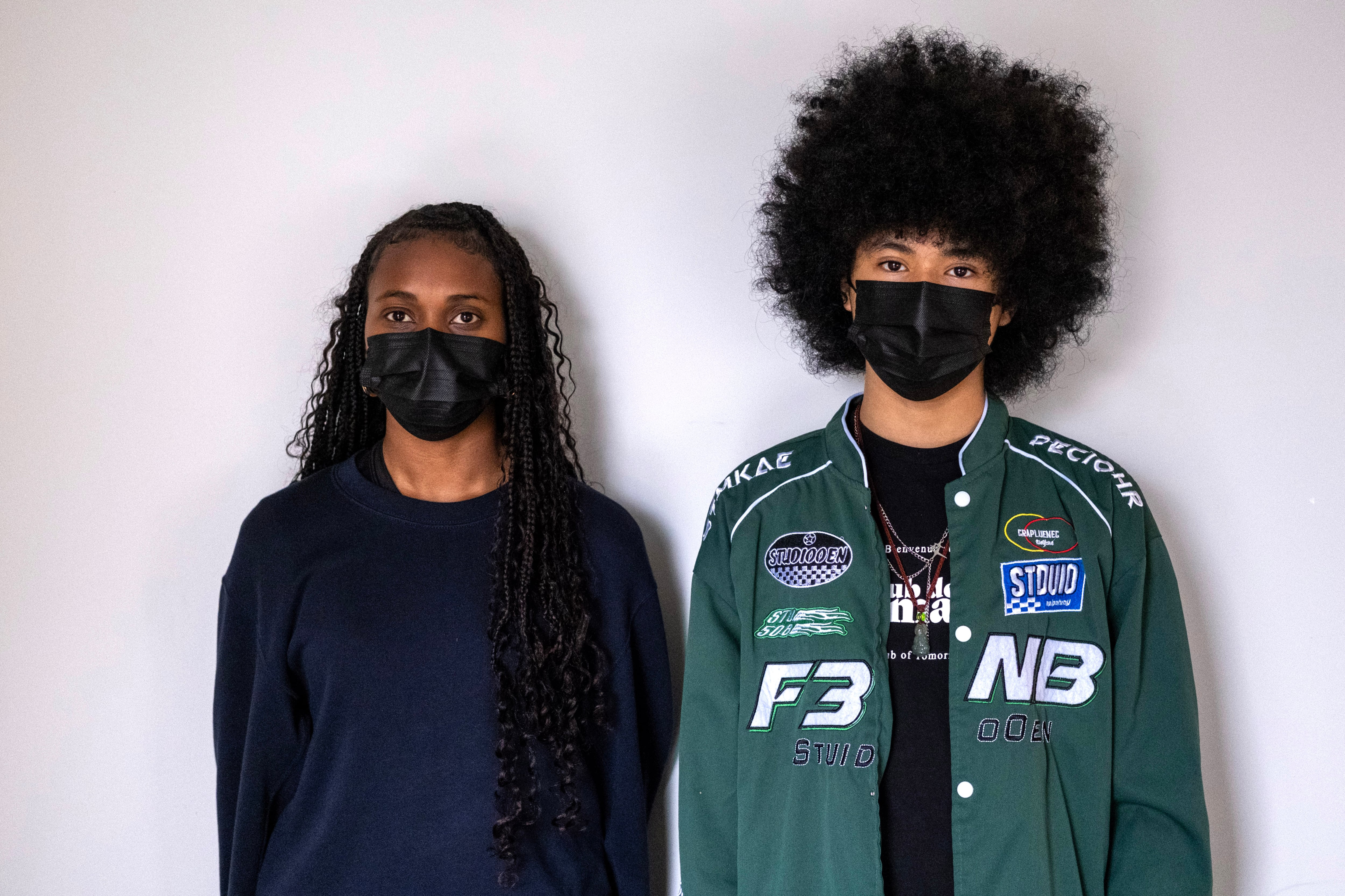 A girl and a boy in a green jacket wear masks.