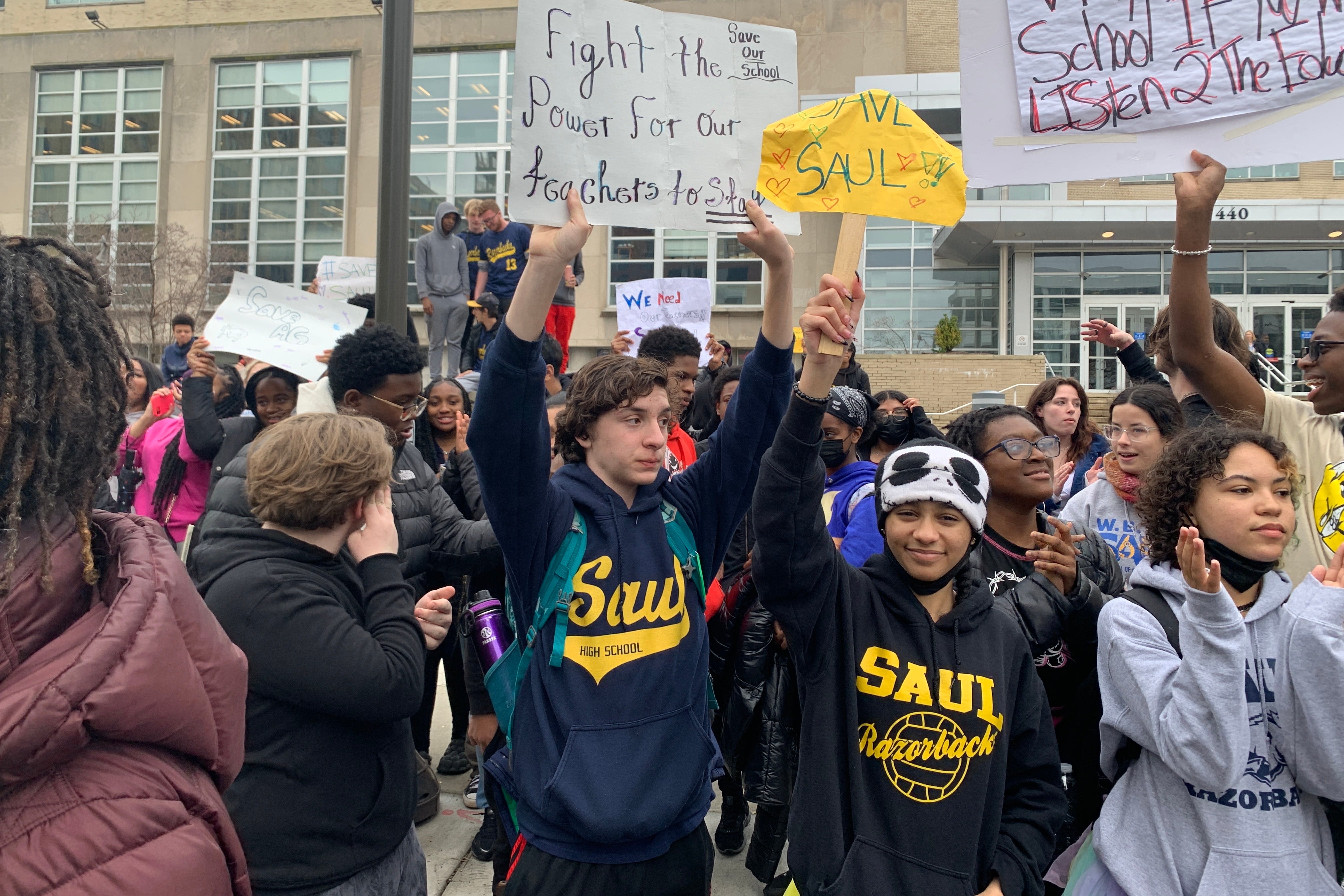 Students hold up signs in front of a brick building