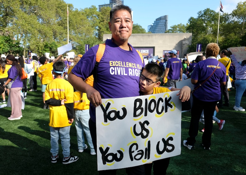 A man in a purple shirt and a boy in a yellow shirt hold a sign.