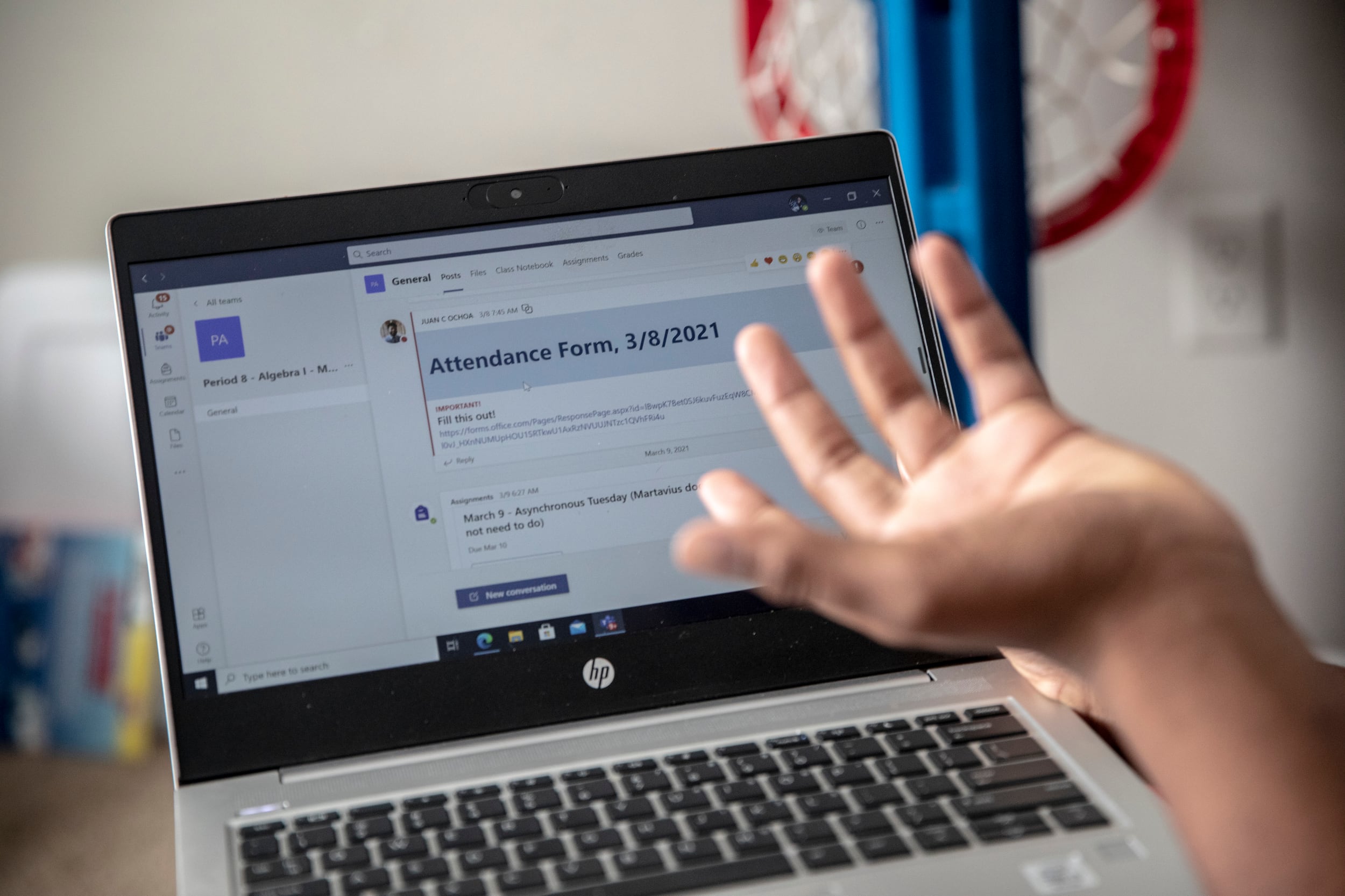 The hand of a student appears in front of a laptop screen, as they attempt to complete an attendance report for that day of virtual learning.
