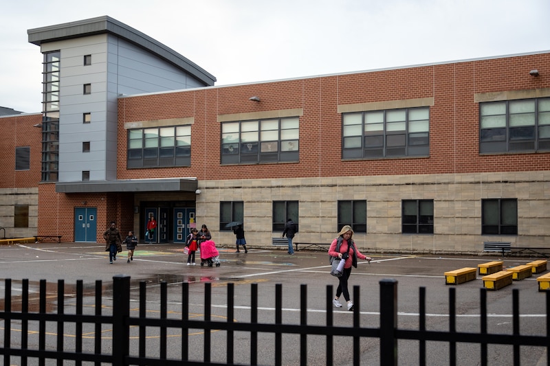 Students and adults walk outside of an entrance of a school.