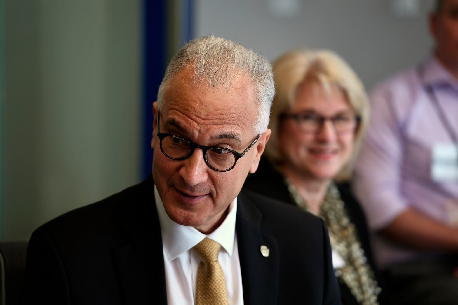 University of Colorado System President Mark Kennedy smiles as he looks down. Kennedy, dressed in black jacket and gold tie wears a CU pin on his lapel.