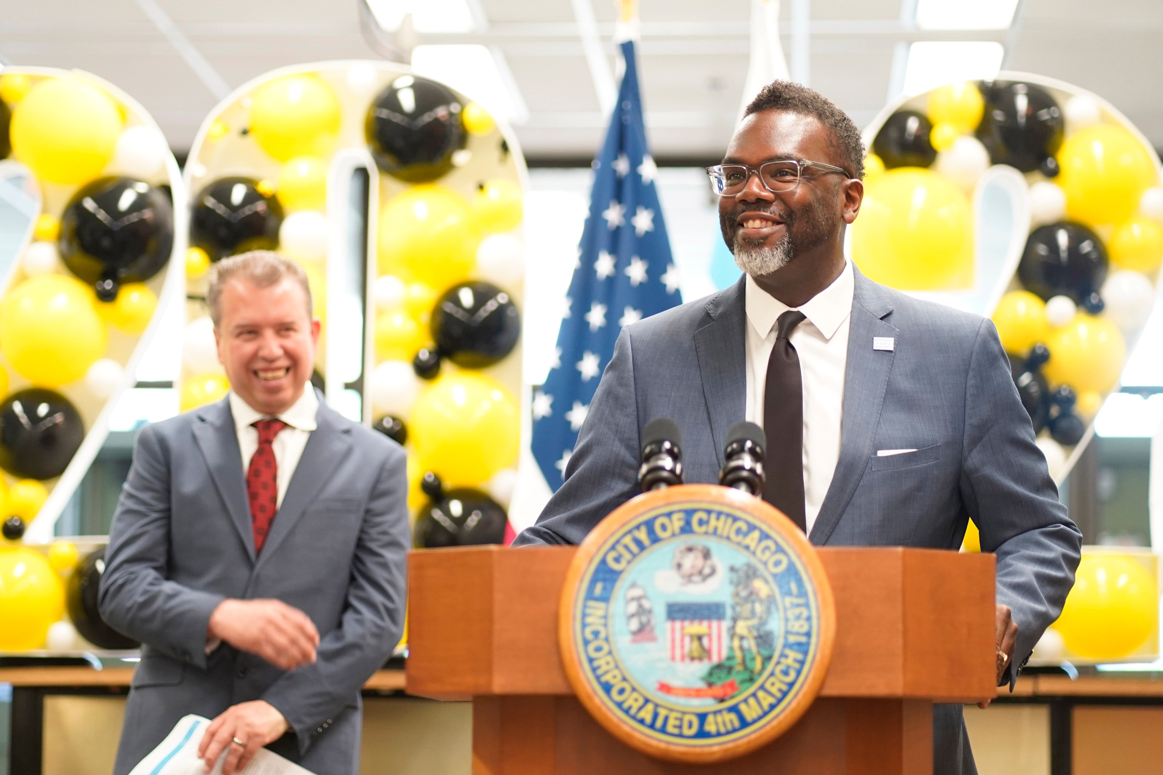 A man in a gray suit jacket stands at a podium