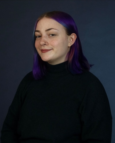 Headshot of a teenage girl wearing a black turtleneck. Her hair is dyed purple.